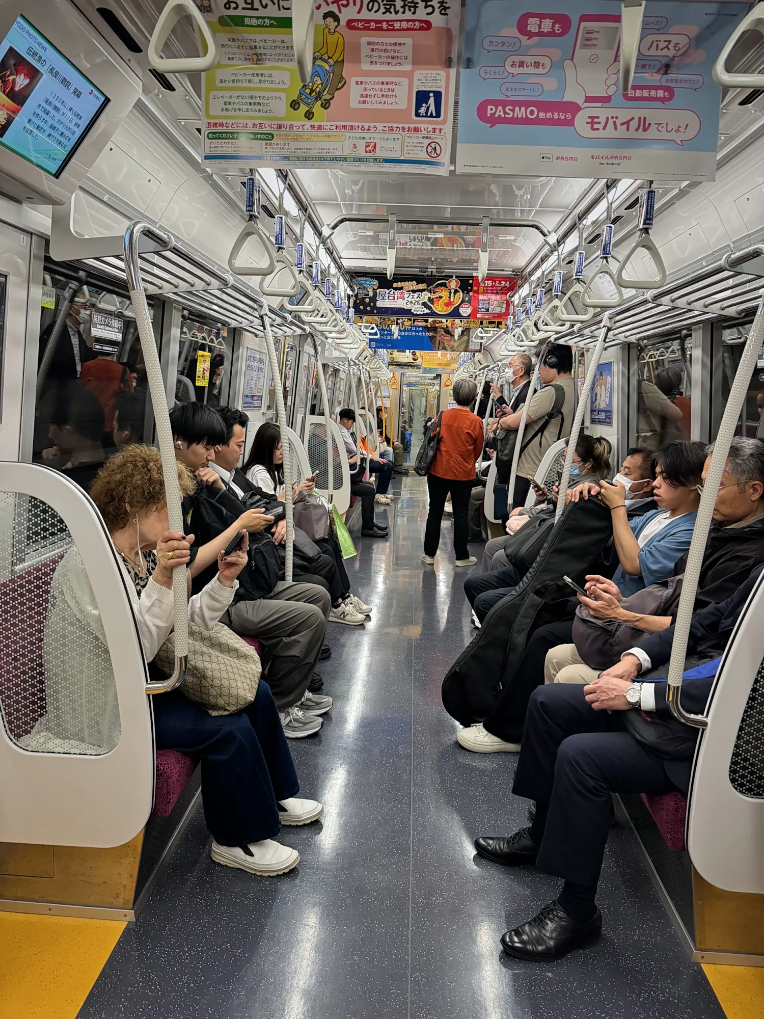 Passengers sitting quietly on padded bench seats inside a clean Tokyo subway car, with straps hanging from the rails.