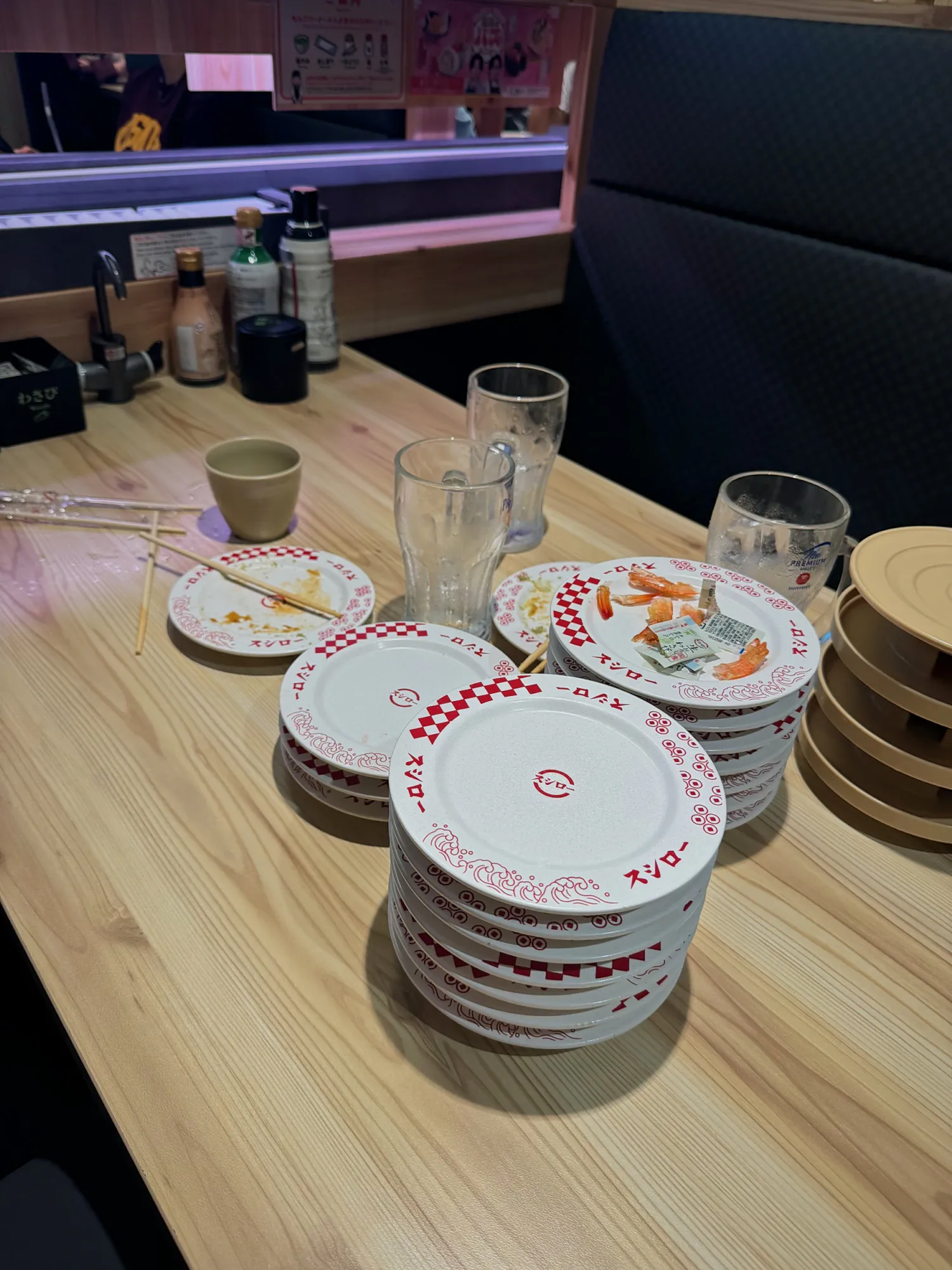 Stacks of empty red-and-white Sushiro plates and glasses on a wooden table at Sushiro in Tokyo.