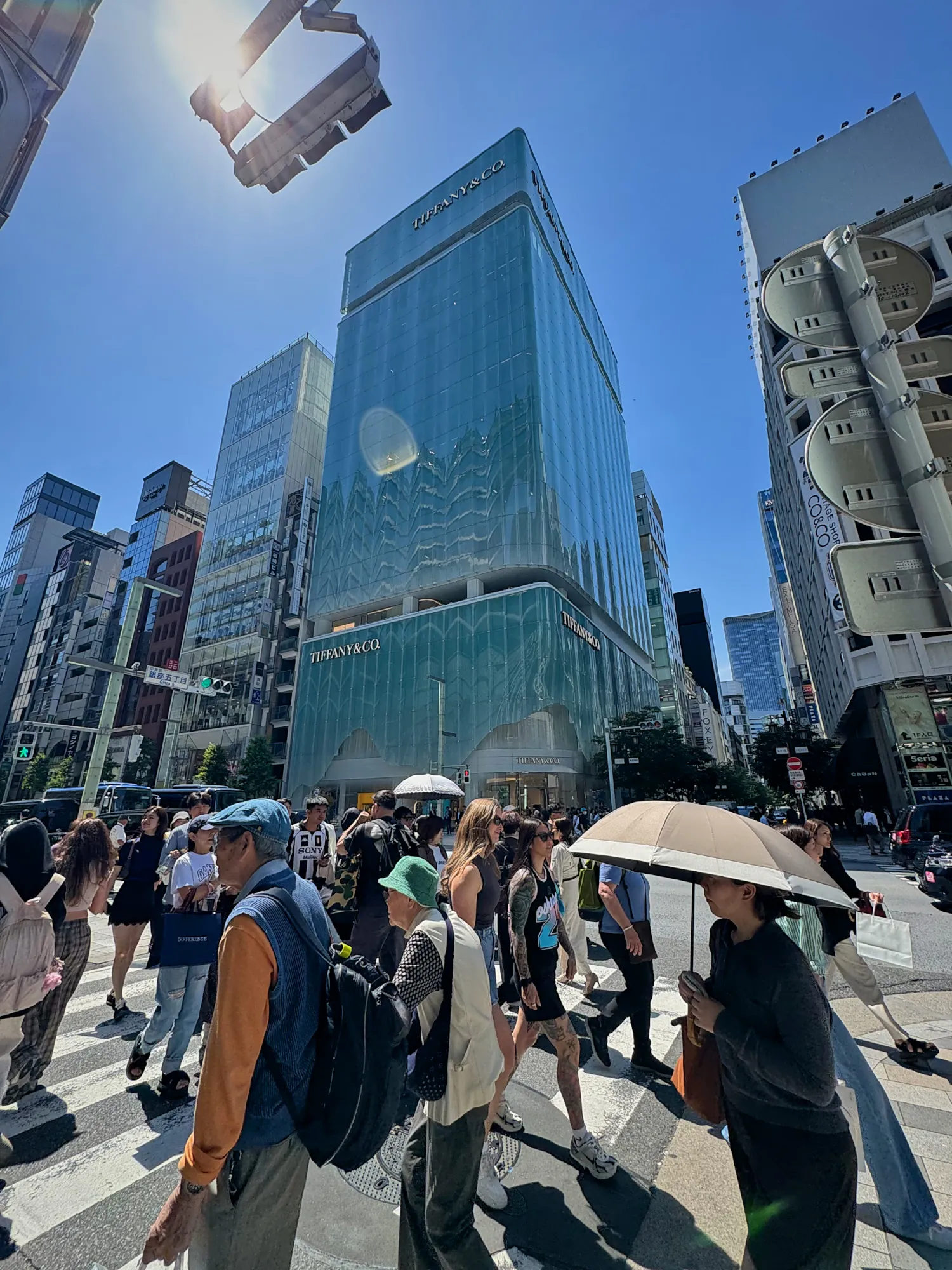 The glass Tiffany & Co. building at a busy, sunny intersection in Ginza, Tokyo.