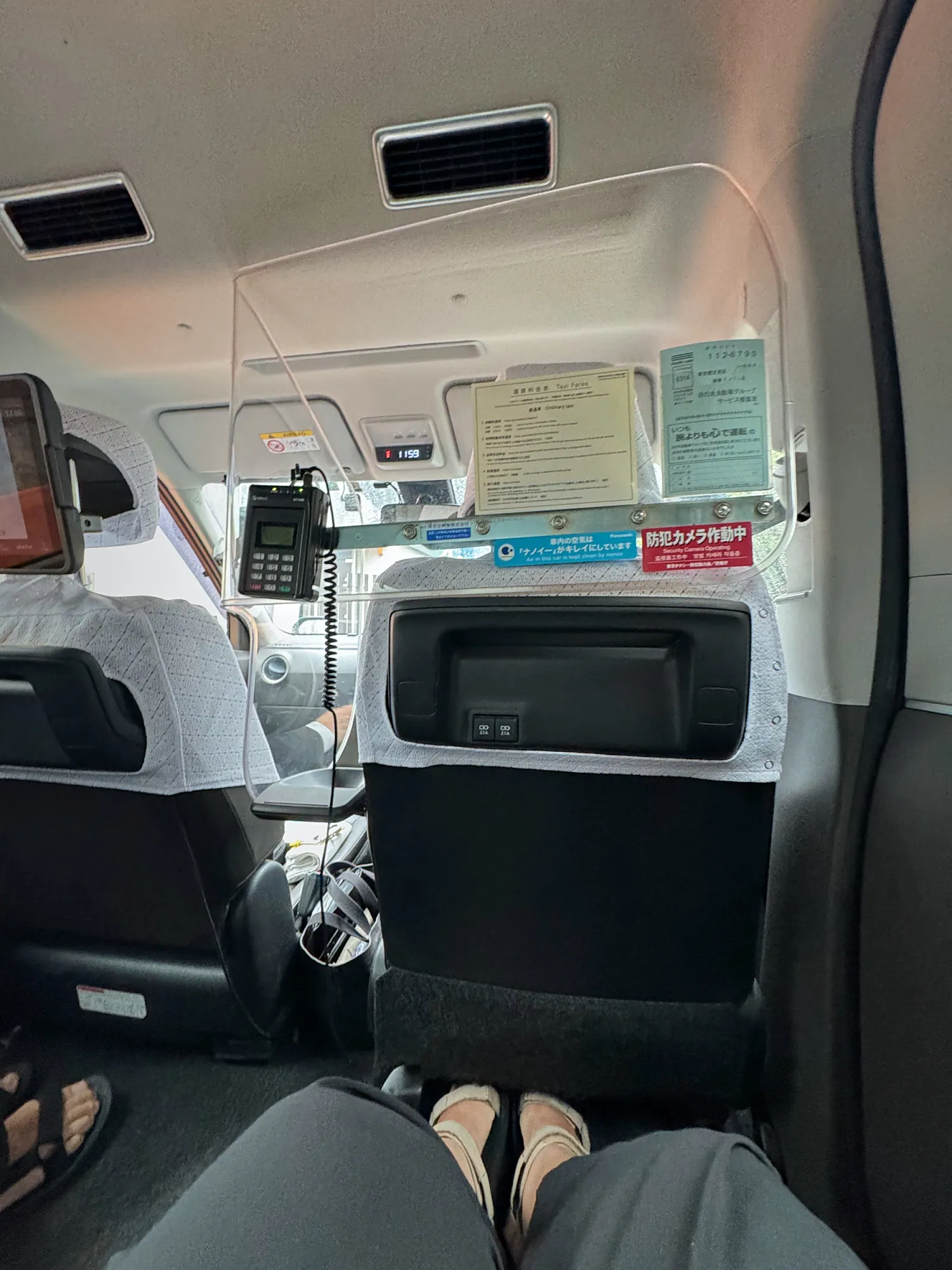 The roomy back seat of a Tokyo taxi, looking toward the partition and the screen on the seatback ahead.