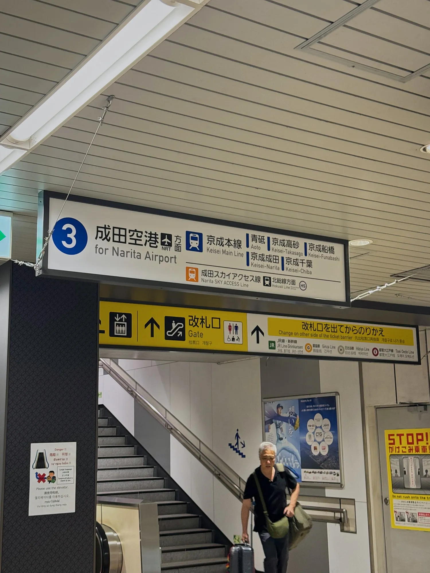 A blue overhead sign pointing to the Narita Airport trains, with stairs leading down to the platform.