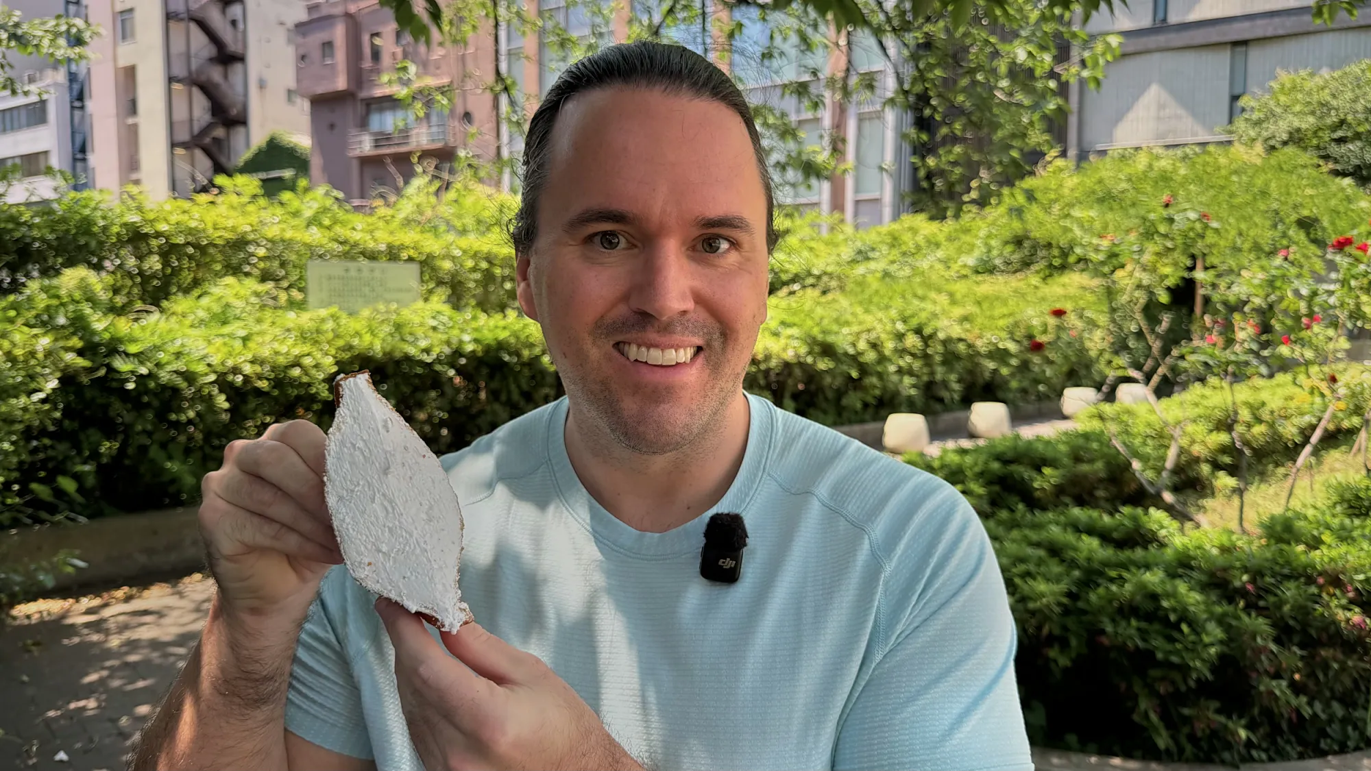 Cream smiling and holding up the Age.3 whipped cream fried sandwich in front of a hedge in Ginza.