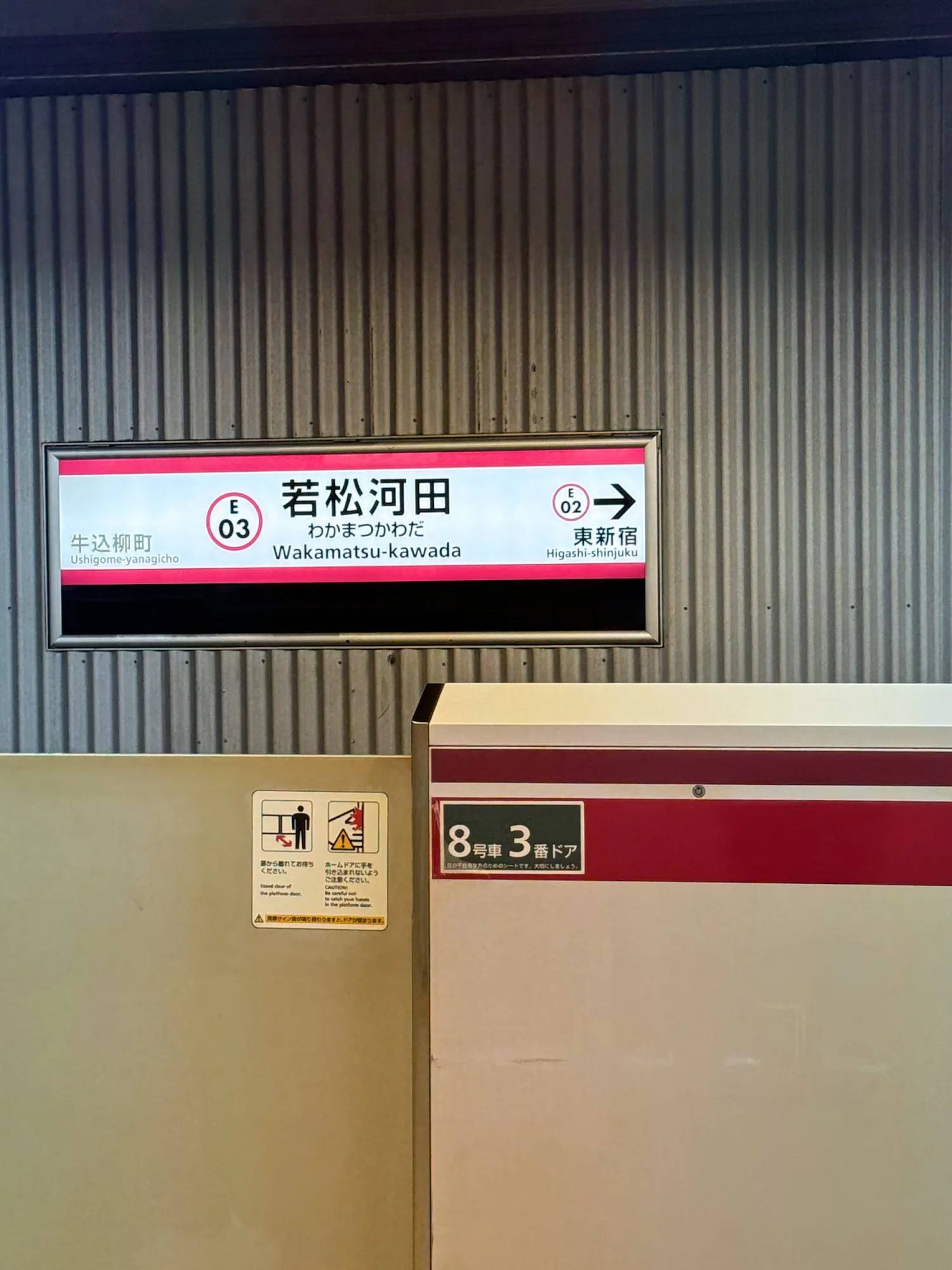 A Wakamatsu-kawada station name sign on the Oedo Line platform, showing the code E03 and an arrow to the next station, Higashi-shinjuku, E02.