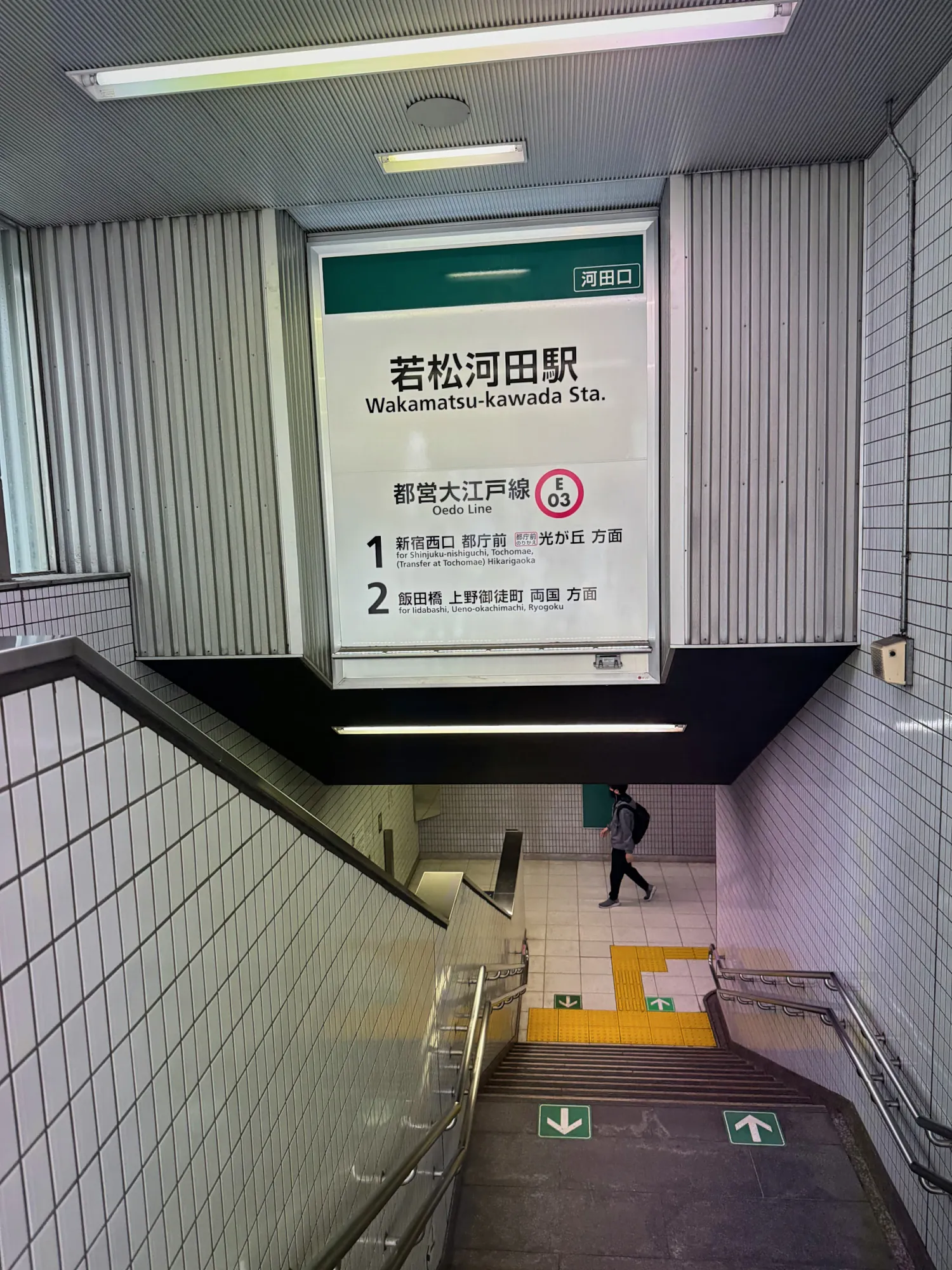 The entrance sign for Wakamatsu-kawada Station on the Toei Oedo Line, listing platform 1 and platform 2 destinations above a staircase going down.