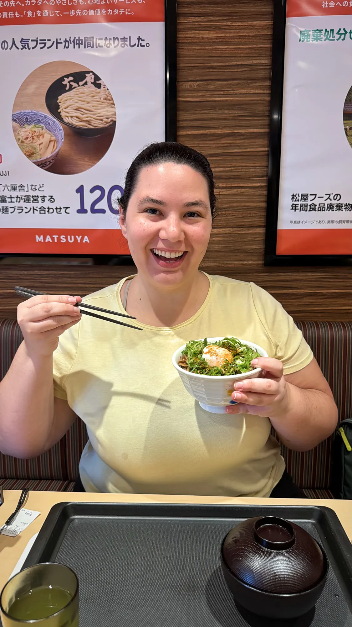 Bernie smiling as she holds up a bowl of gyudon with green onion and egg at Matsuya