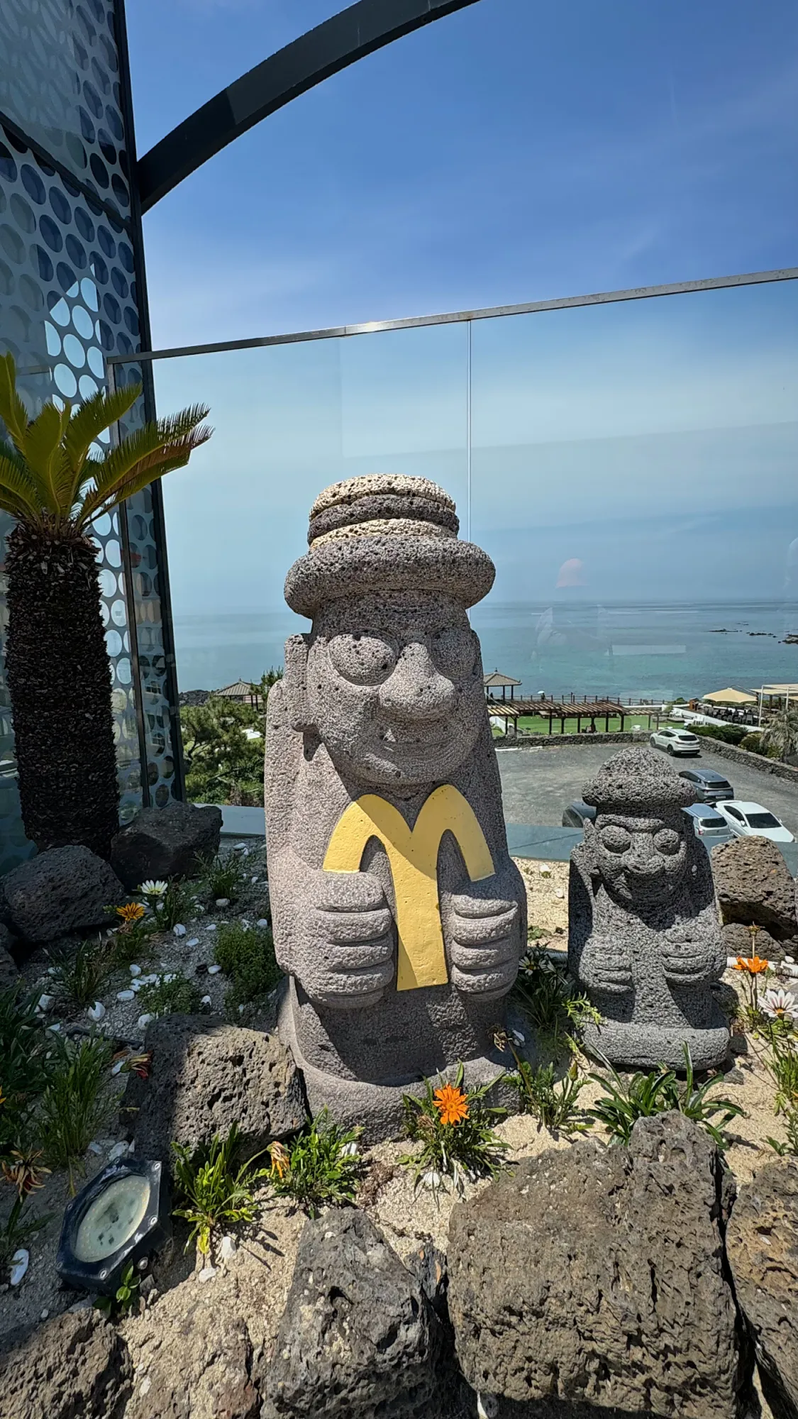 A dol hareubang stone statue holding a small golden arch at a McDonald's on Jeju Island, South Korea.