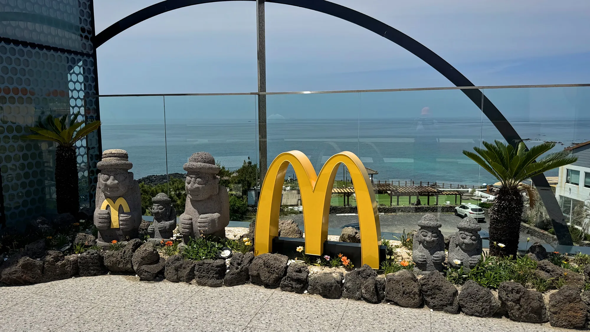 Golden arches and dol hareubang stone statues on the ocean-view rooftop of a McDonald's on Jeju, South Korea.