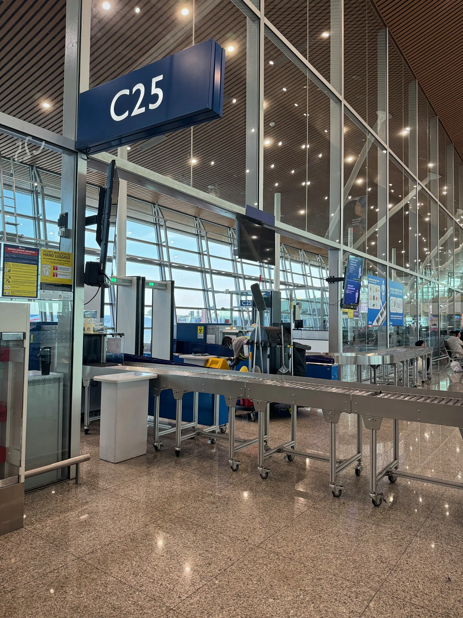 Airport boarding gate C25 with security conveyors and large windows, where we waited for our Malaysia Airlines flight.