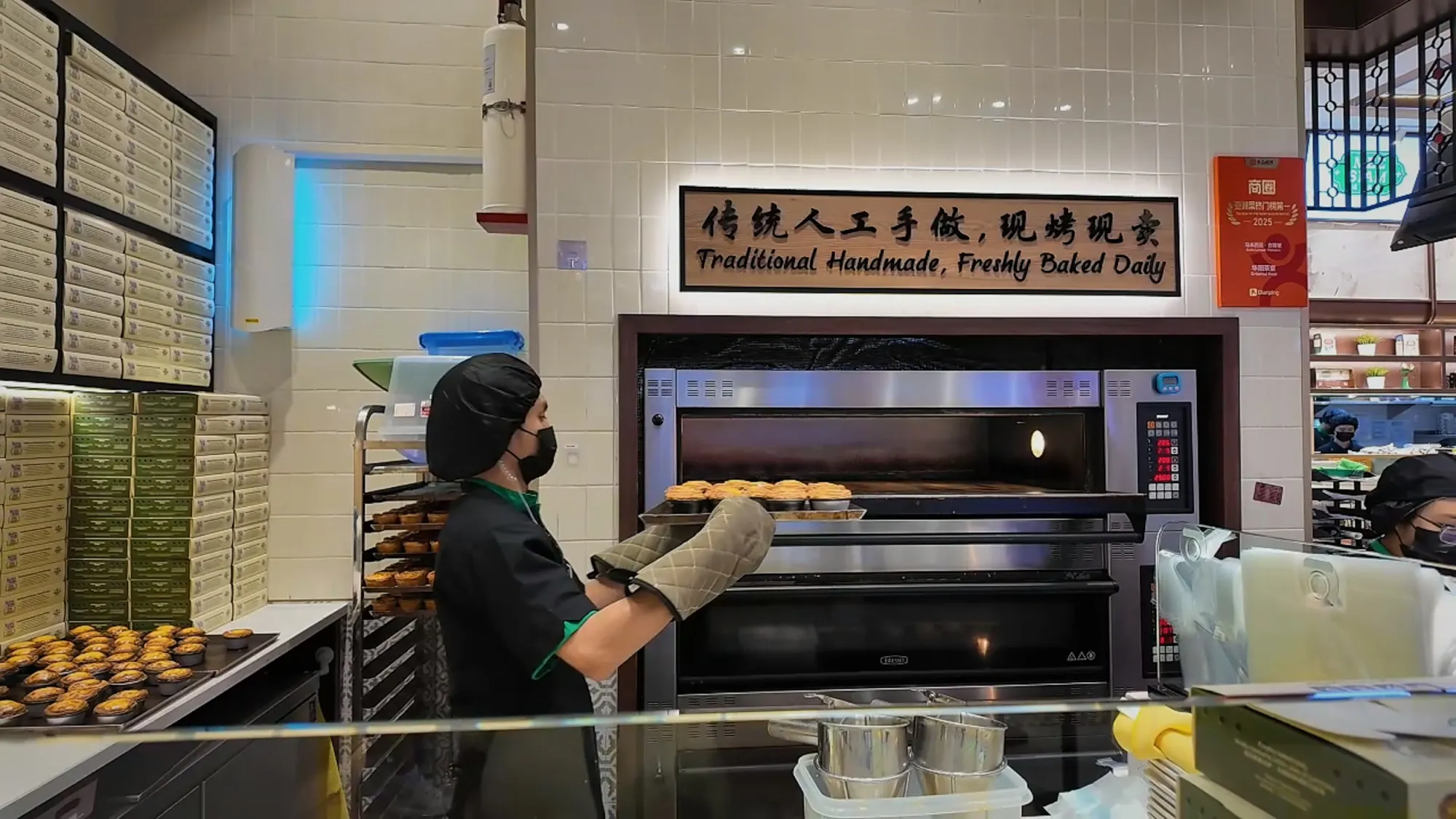 A staff member at Oriental Kopi taking a tray of freshly baked egg tarts from the oven.