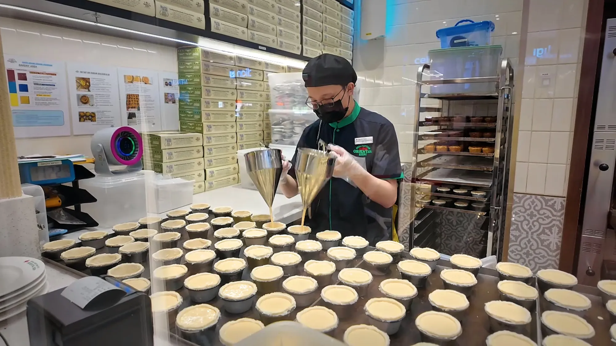 A staff member at Oriental Kopi filling rows of egg tart shells with custard.