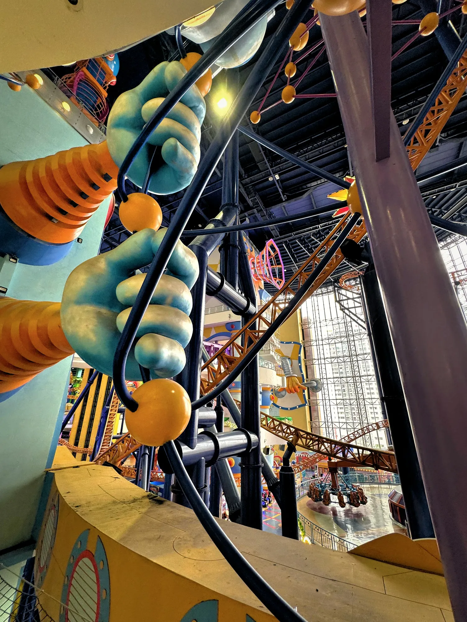 Giant blue hand sculptures and yellow beads framing the indoor roller coaster track at Berjaya Times Square Theme Park.