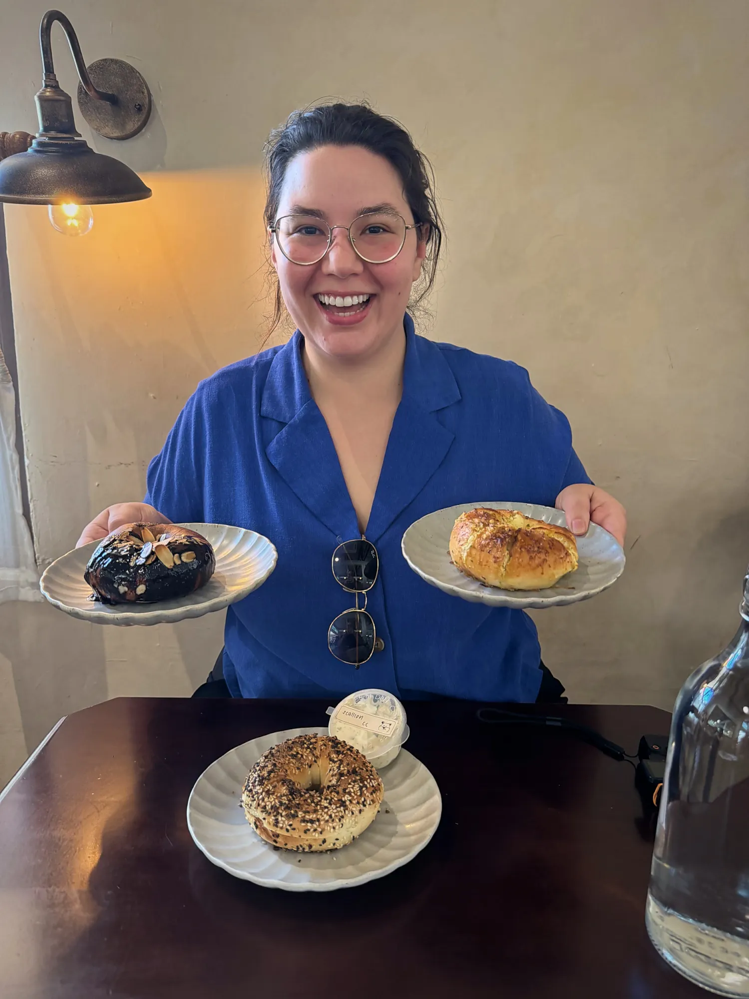 Bernie smiling and holding up the chocolate almond bagel and the garlic bagel, with an everything bagel on the table at Grumpy Bagels, Kuala Lumpur.