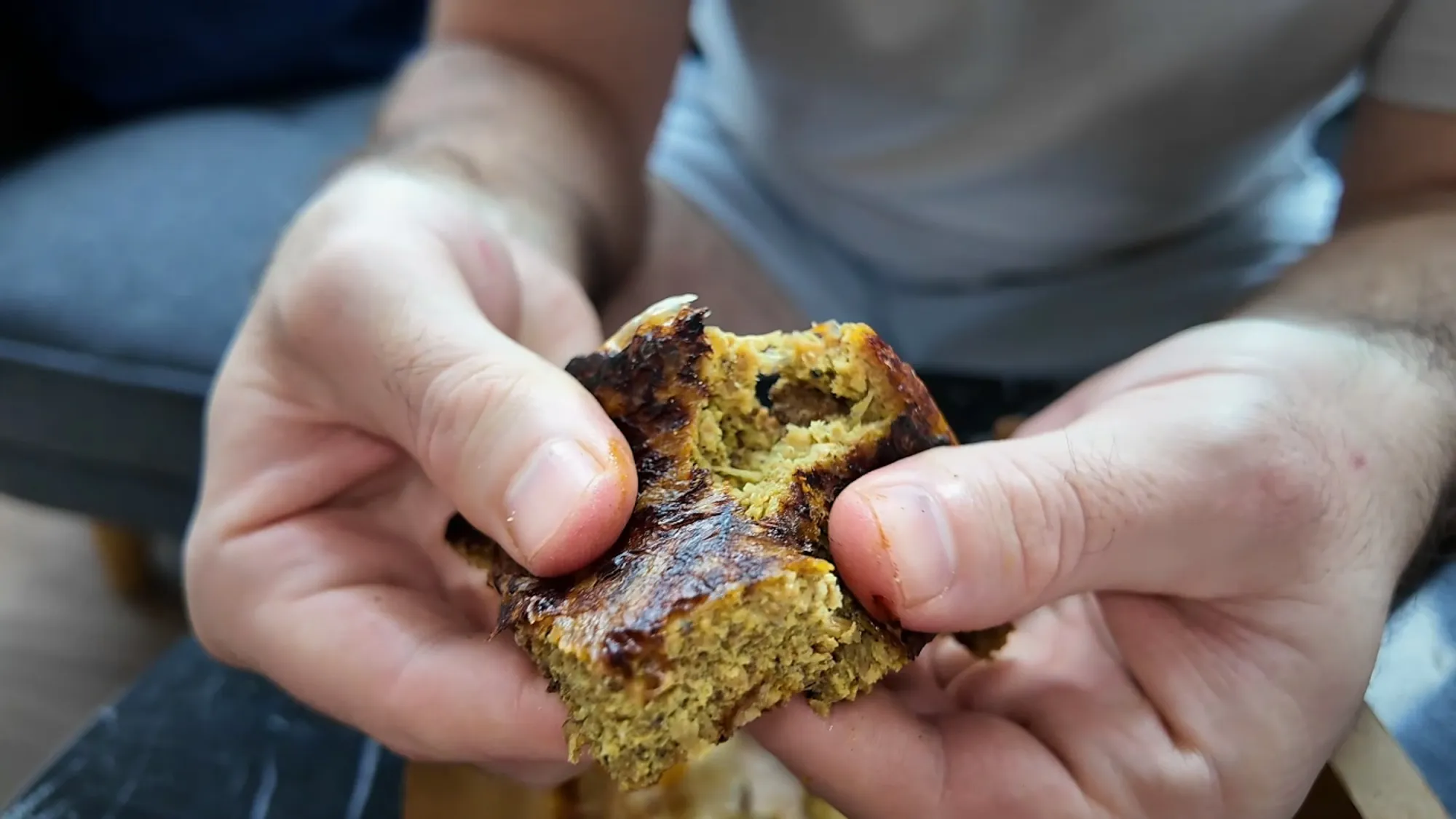 Cream breaking open a piece of murtabak daging to show the spiced minced beef and egg filling inside the crisp roti
