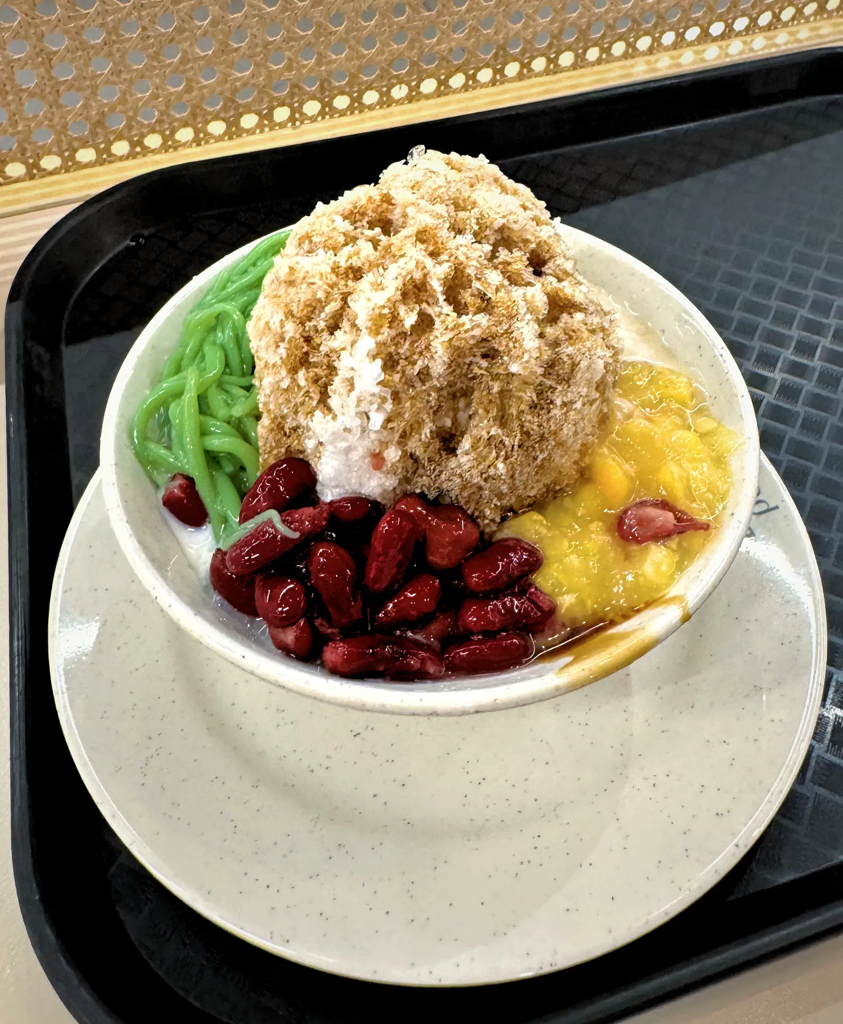 Shaved ice drizzled with gula melaka palm sugar, with green pandan jelly, red beans, and sweet corn in a bowl in Kuala Lumpur