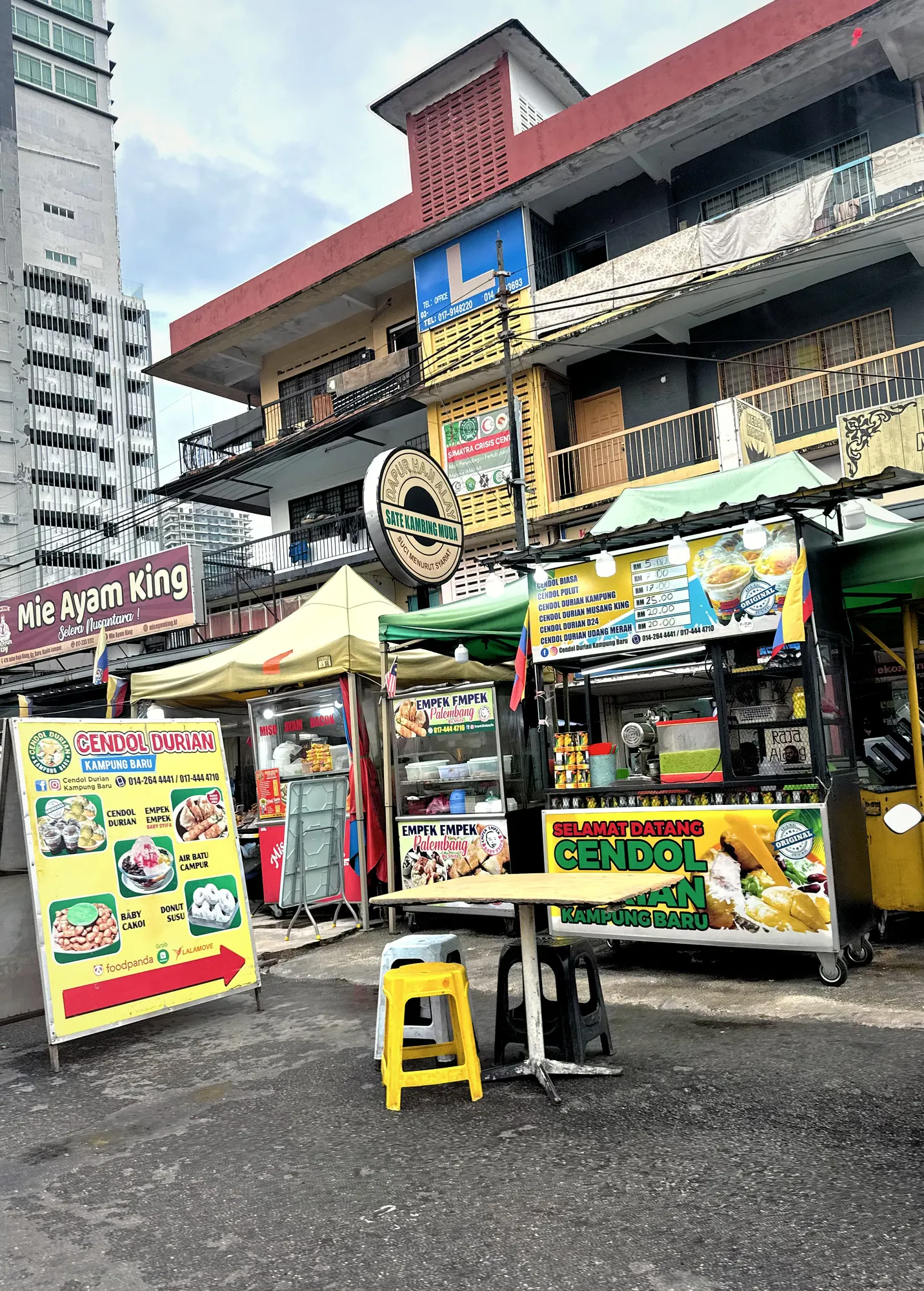 Street food stalls with bright signs for Cendol Durian Kampung Baru and Empek Empek Palembang in Kuala Lumpur, the kind of stall where you pay cash.