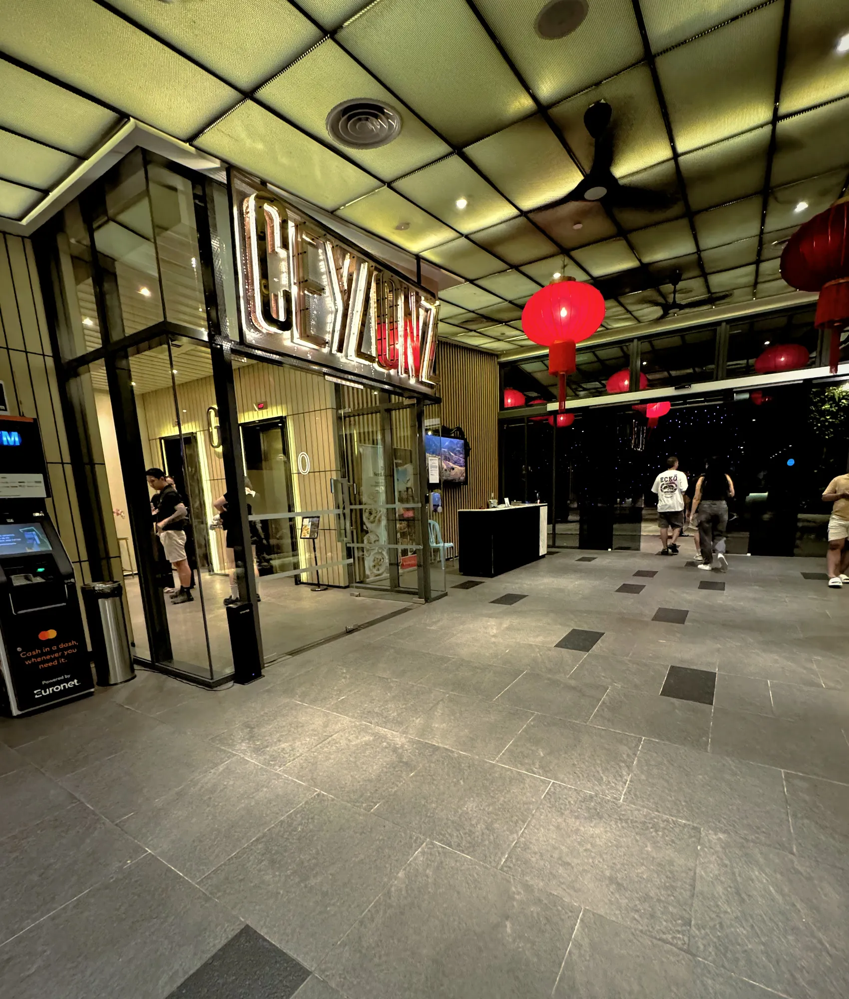 The lit glass entrance lobby of Ceylonz Suites in Kuala Lumpur at night, decorated with red lanterns.