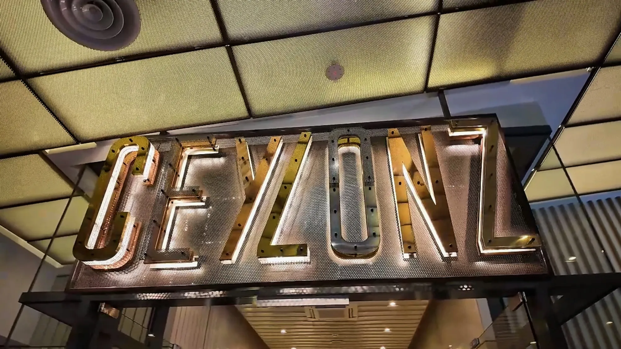 The lit metal Ceylonz sign hanging from the ceiling at the entrance of Ceylonz Suites in Kuala Lumpur.