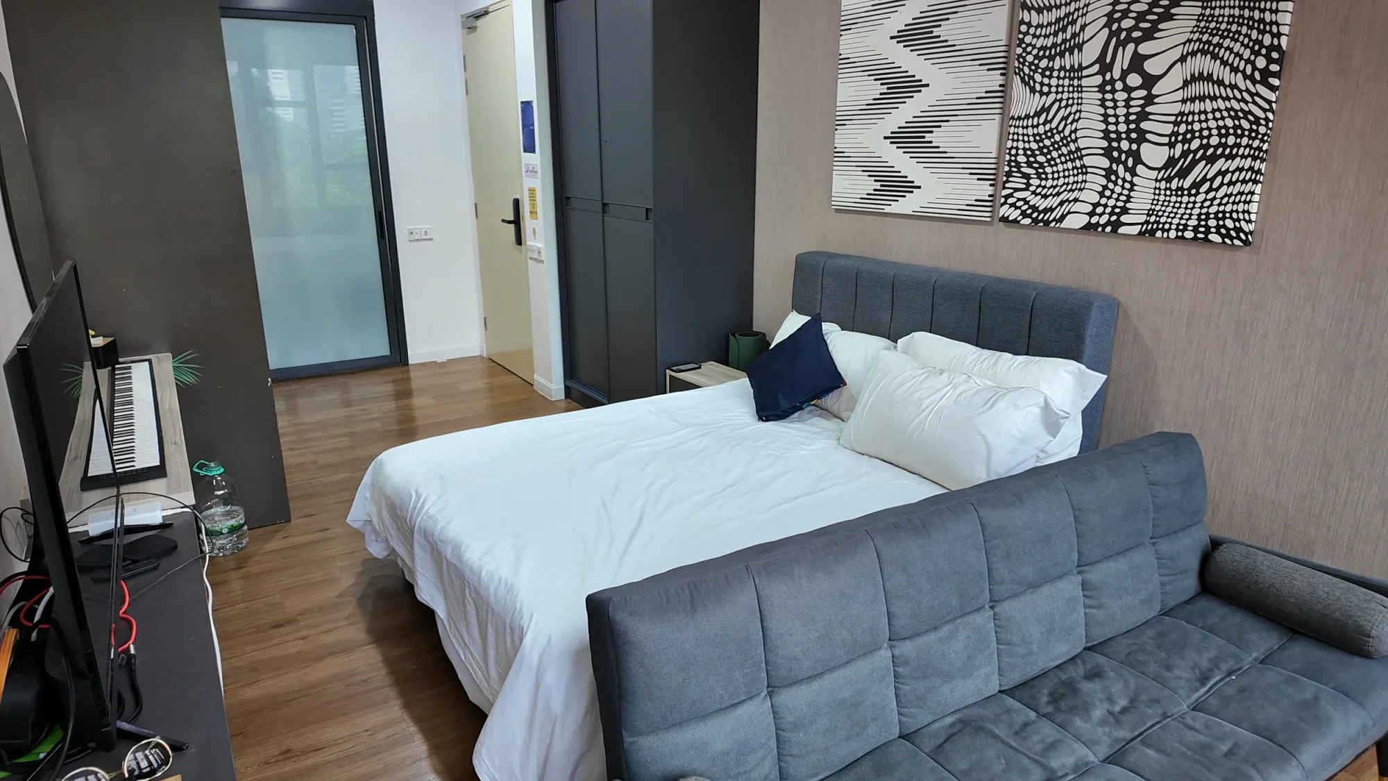 The king bed and grey couch in our studio at Ceylonz Suites, with wood floors and a frosted glass bathroom door.
