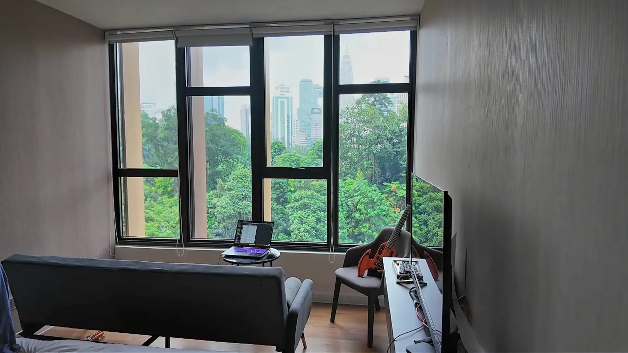 The living area of our studio at Ceylonz Suites in Kuala Lumpur, with a sofa, a small laptop table, and big windows over trees and skyscrapers.