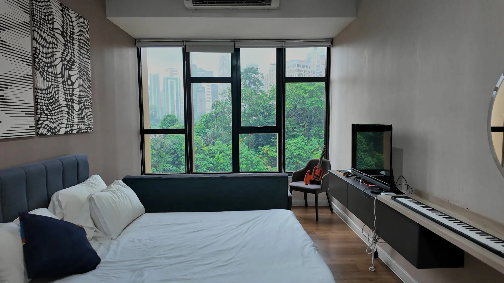 The king bed in our studio at Ceylonz Suites facing big windows full of trees and skyscrapers.