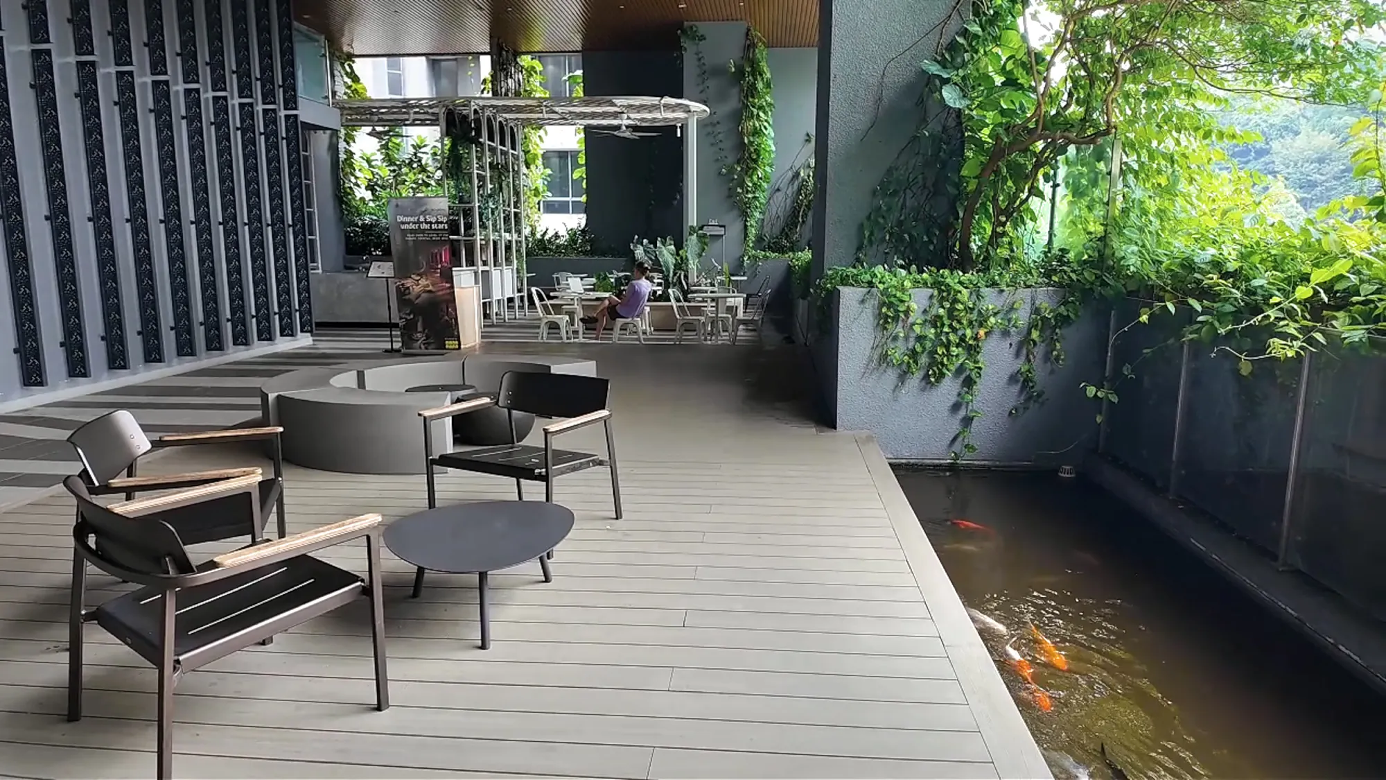 A covered rooftop lounge at Ceylonz Suites with armchairs, plants, and a koi pond along one side.