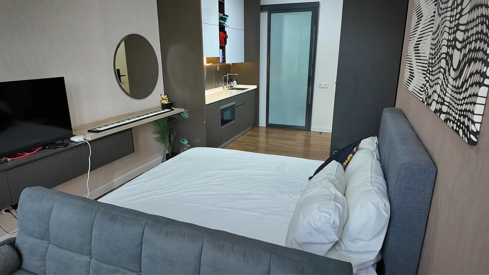 Our studio at Ceylonz Suites in Kuala Lumpur, with a king bed, a grey couch at its foot, a TV, and a round mirror.