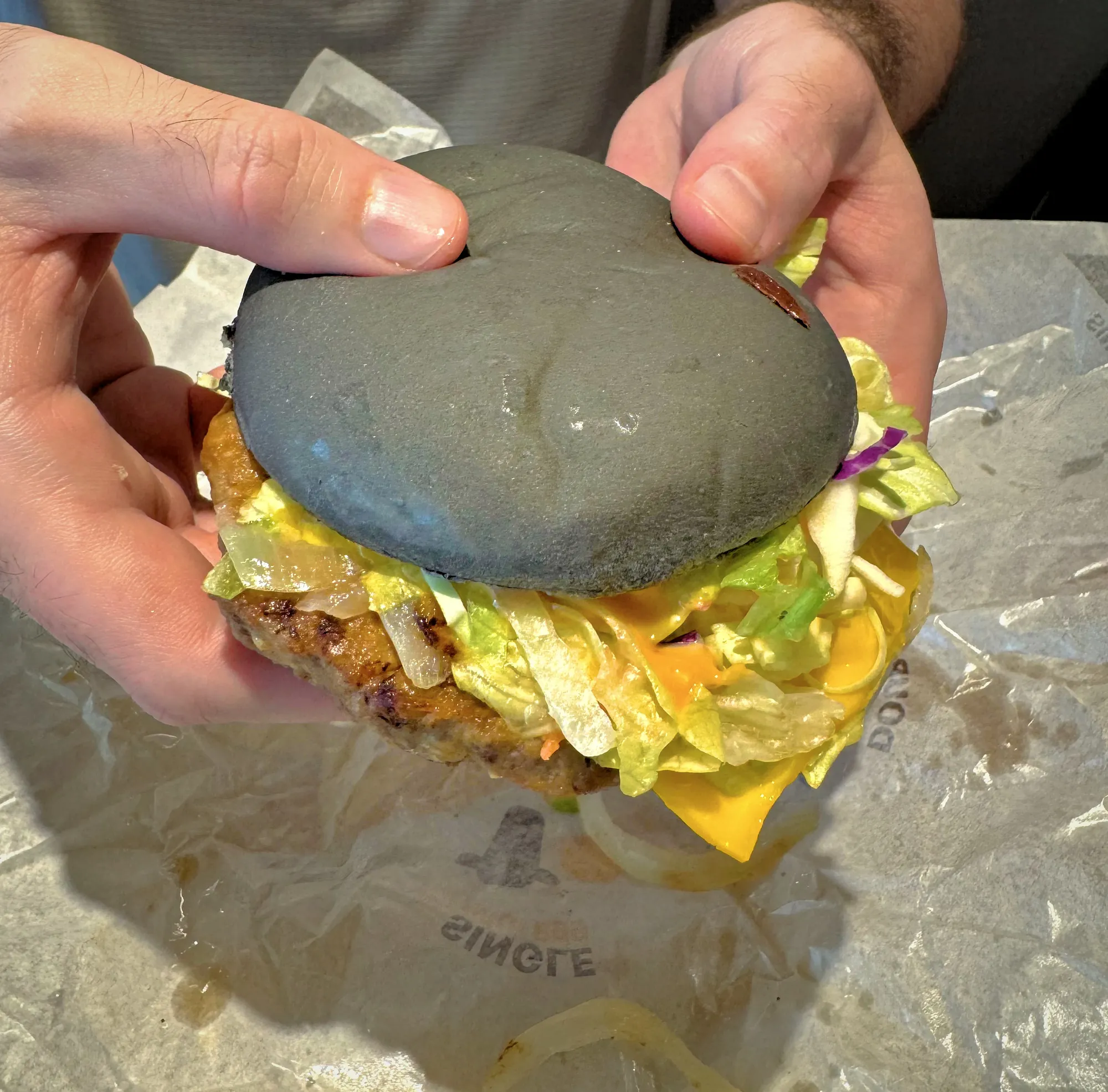 A diner holds a specialty McDonald's burger with a striking jet-black charcoal bun, lettuce, and melted cheese over wrapping paper.