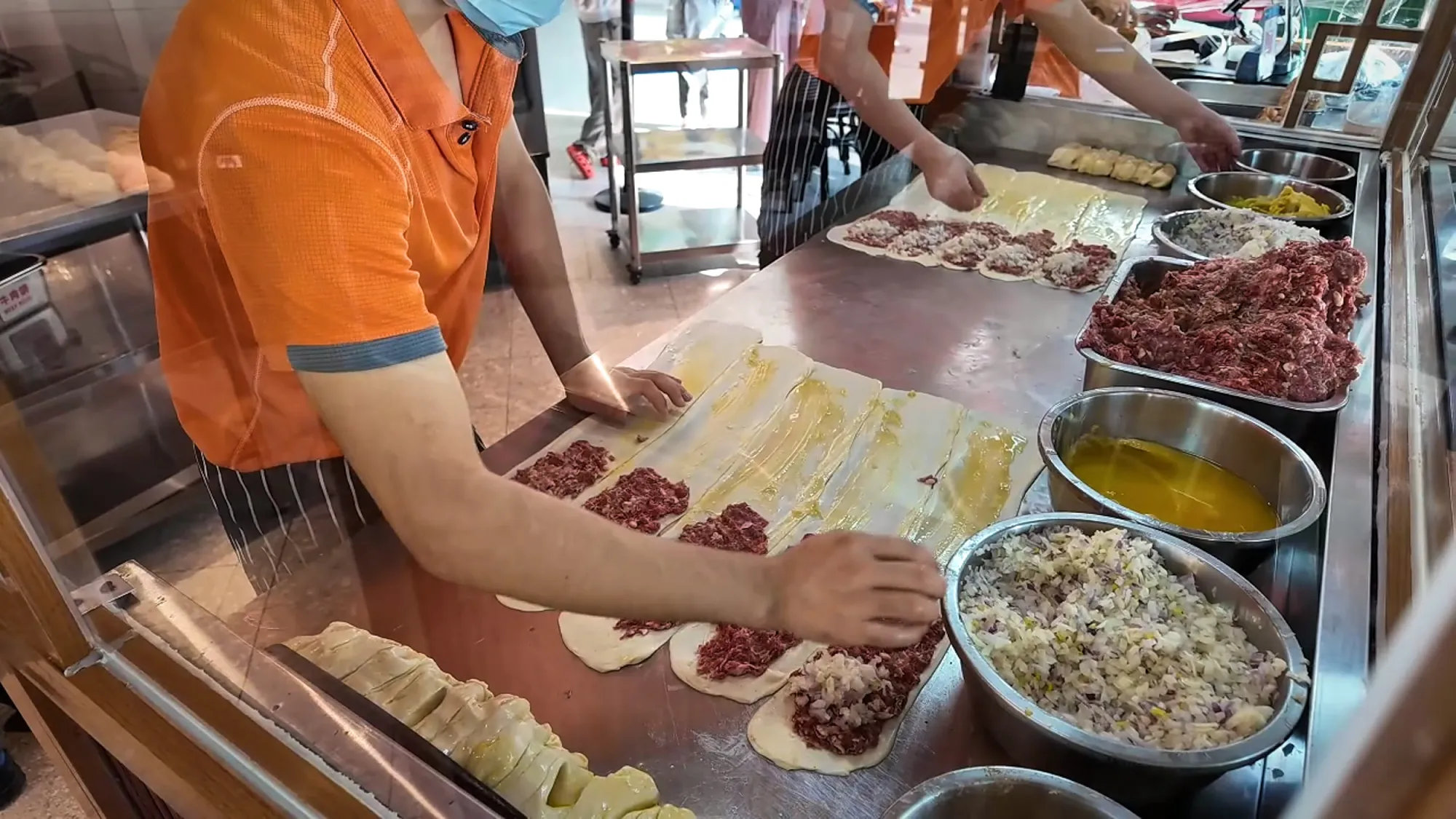 A cook laying minced beef onto strips of thin, buttered dough at Mon Chinese Beef Roti.