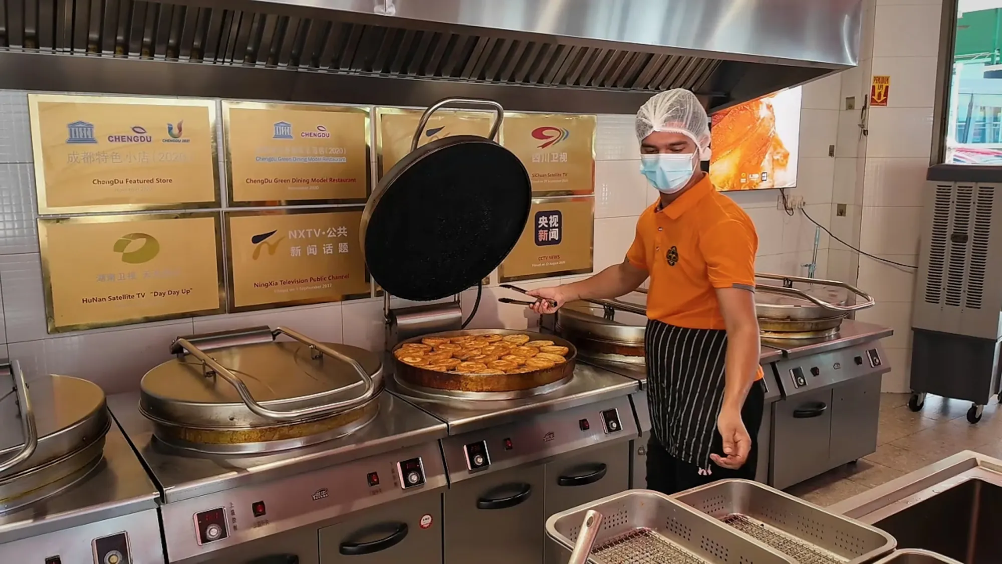 A cook in a hairnet frying roti in large black pans at Mon Chinese Beef Roti.