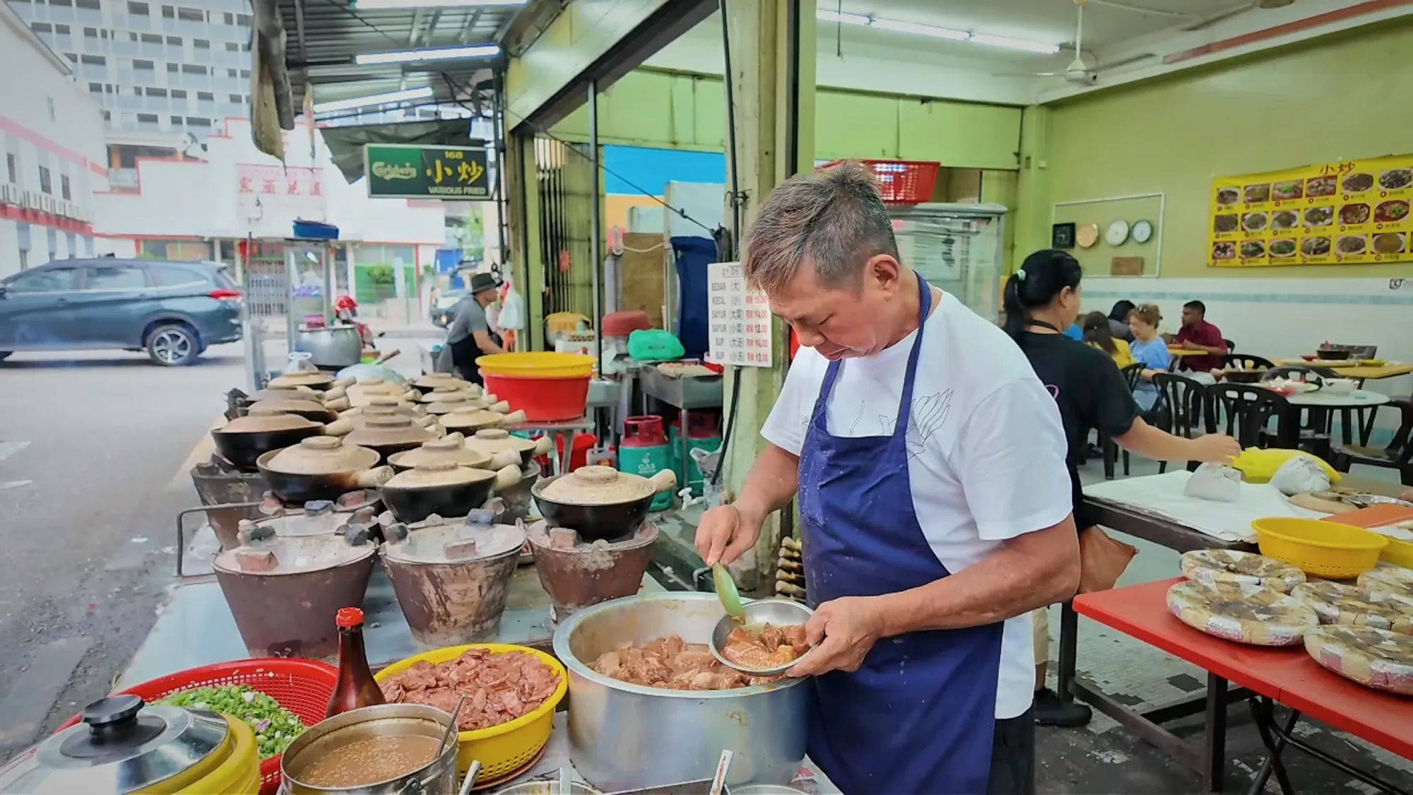 The cook in a blue apron scooping marinated chicken into claypots at the 168 stall in Pudu, Kuala Lumpur.