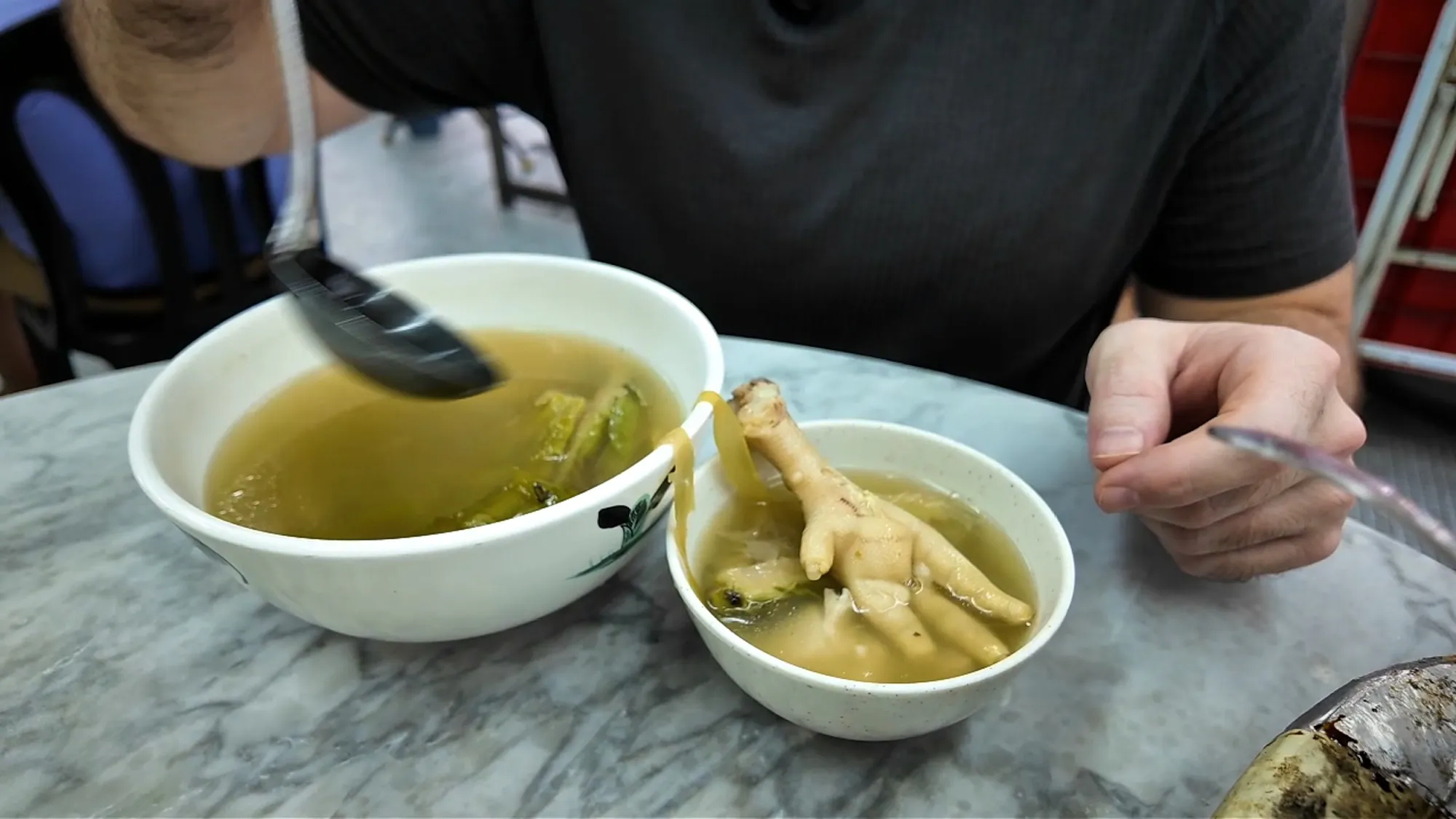 Bowls of chicken soup with chicken feet on a marble table at 168 Claypot Chicken Rice in Kuala Lumpur.