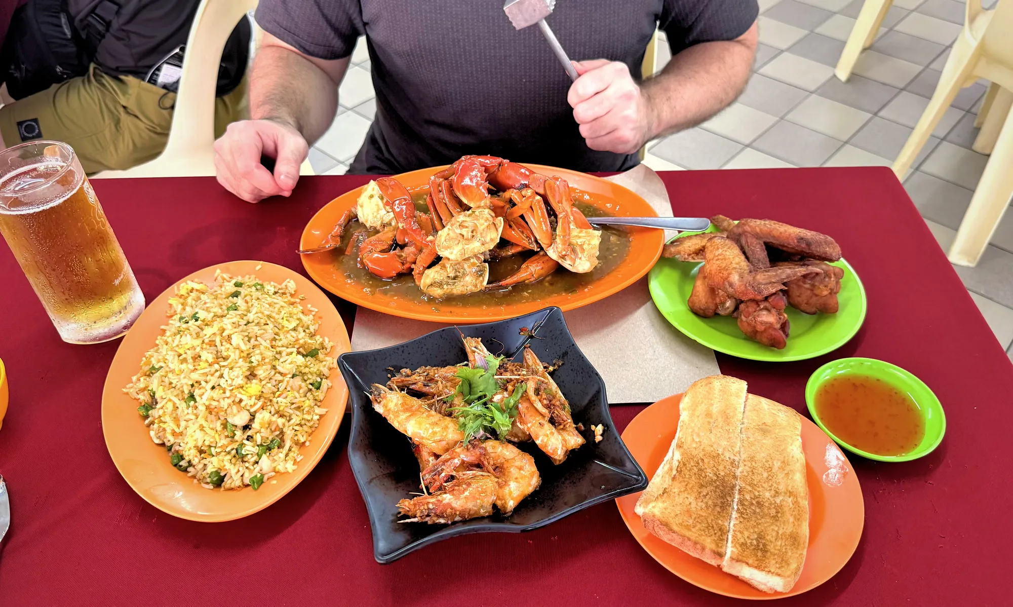 Cream at a red-clothed table with chilli crab, prawns, chicken wings, fried rice, toast, and a beer at Restoran Fatty Crab in Petaling Jaya.