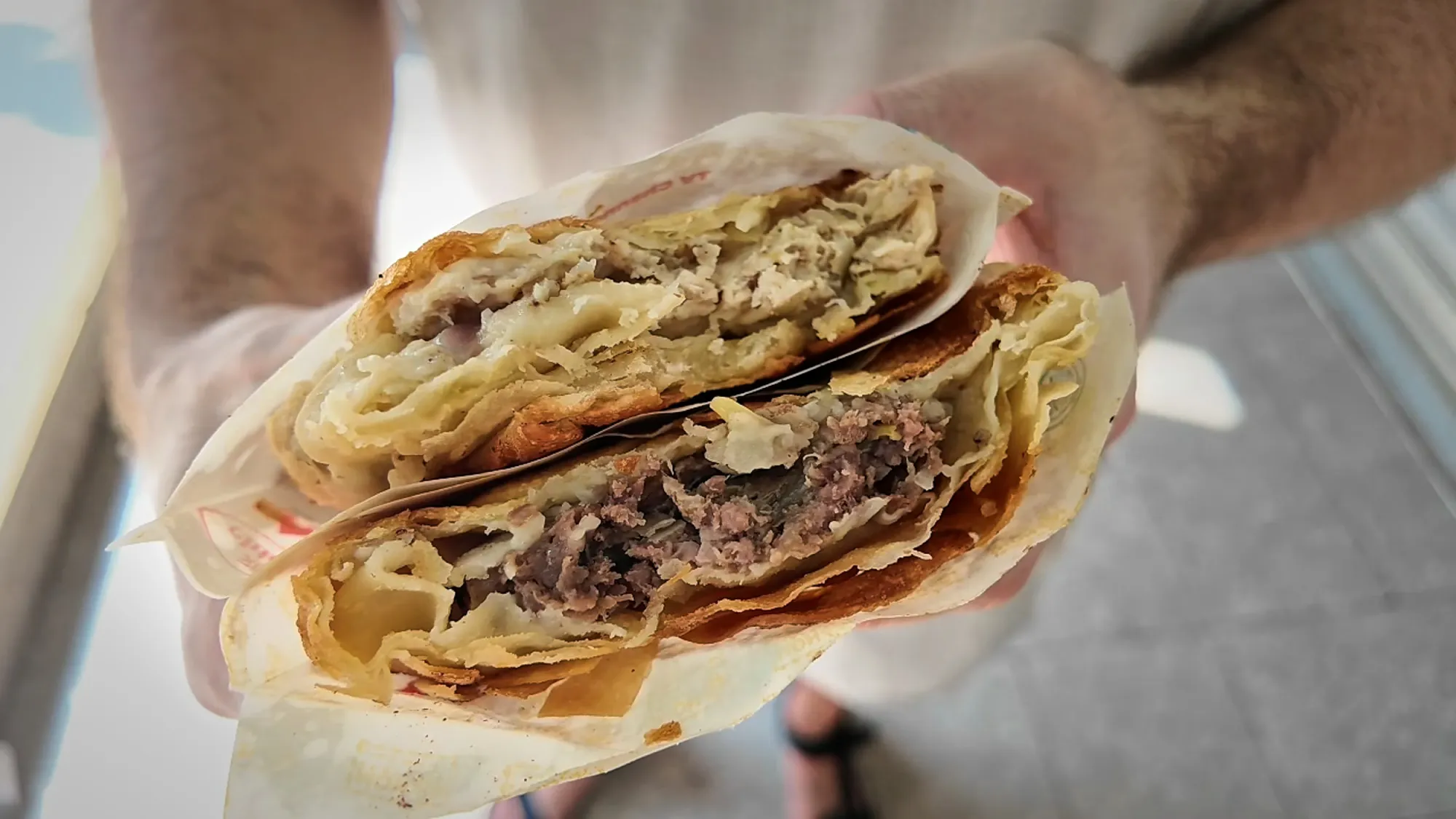 Two halves of a Mon Chinese beef roti held up to show the flaky shell and spiced beef filling