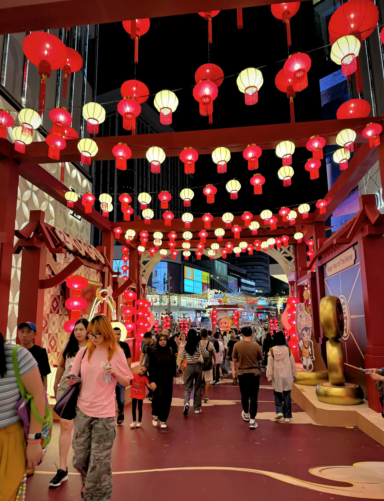 People walking along a red walkway lit by dozens of red and white Chinese New Year lanterns in Bukit Bintang, Kuala Lumpur.