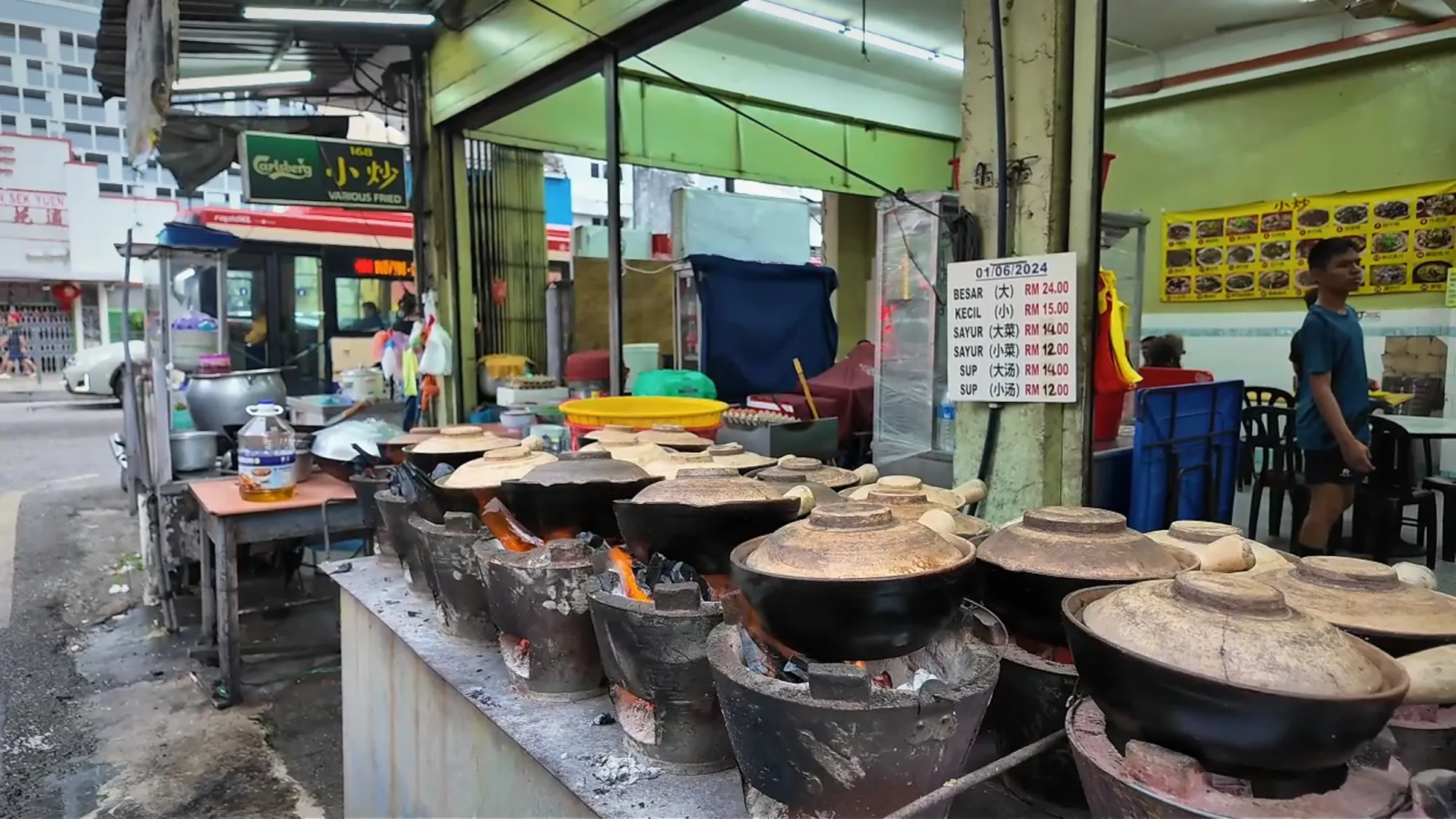 A row of claypots cooking over glowing charcoal stoves at 168 Claypot Chicken Rice in Pudu.