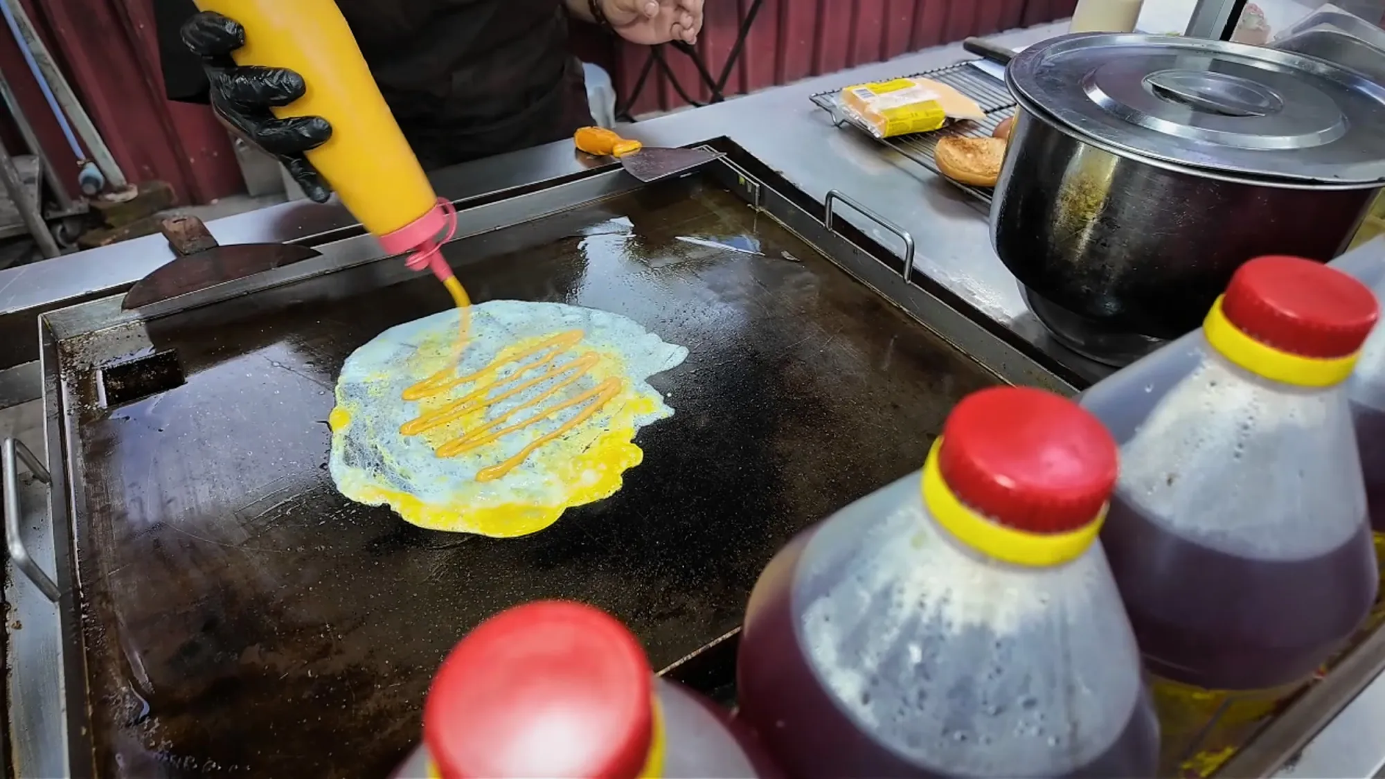 A cook squeezes sauce over a thin layer of egg spread on the flat-top grill at Boss Burger, Jalan Alor, Kuala Lumpur