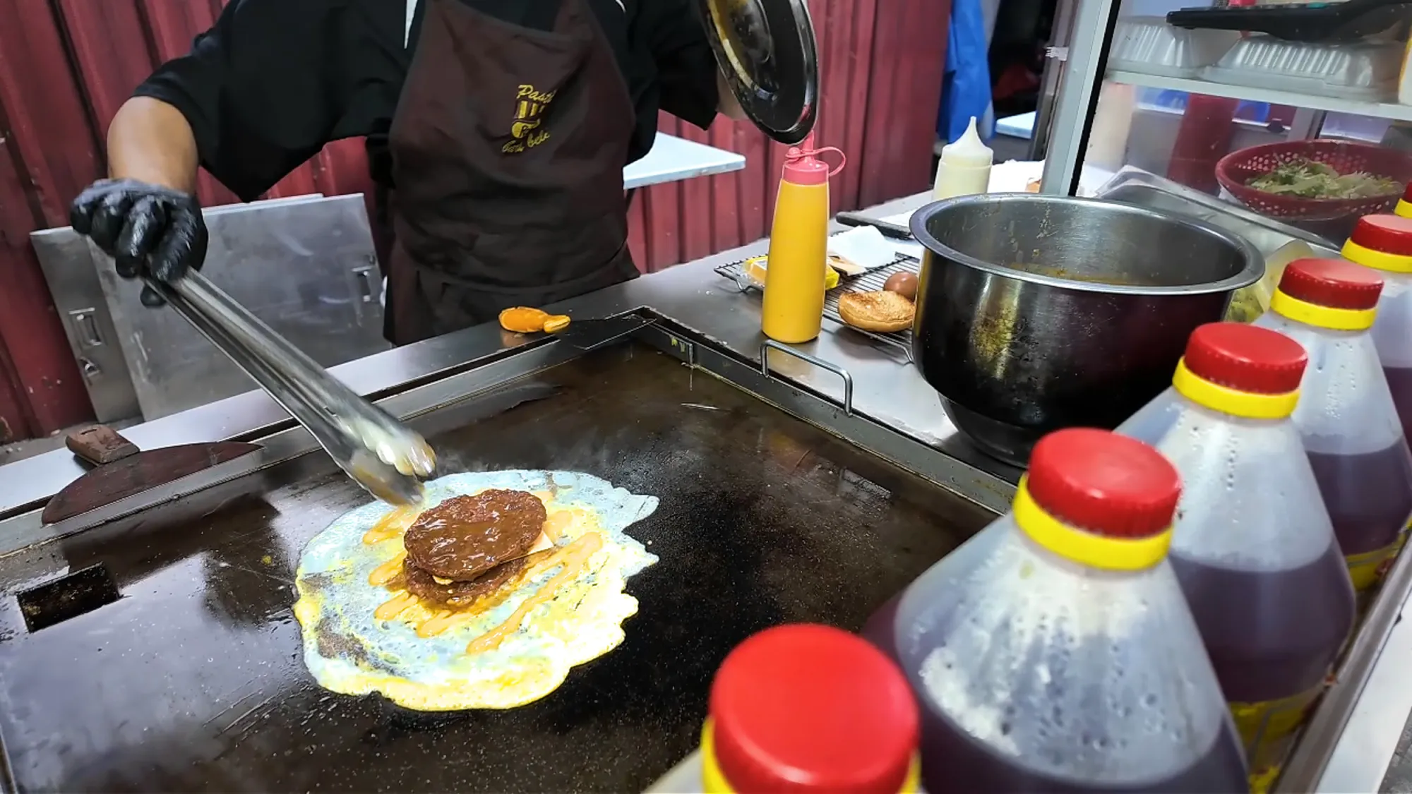 A cook places a Ramly patty on a thin egg on the flat-top grill at Boss Burger, Jalan Alor