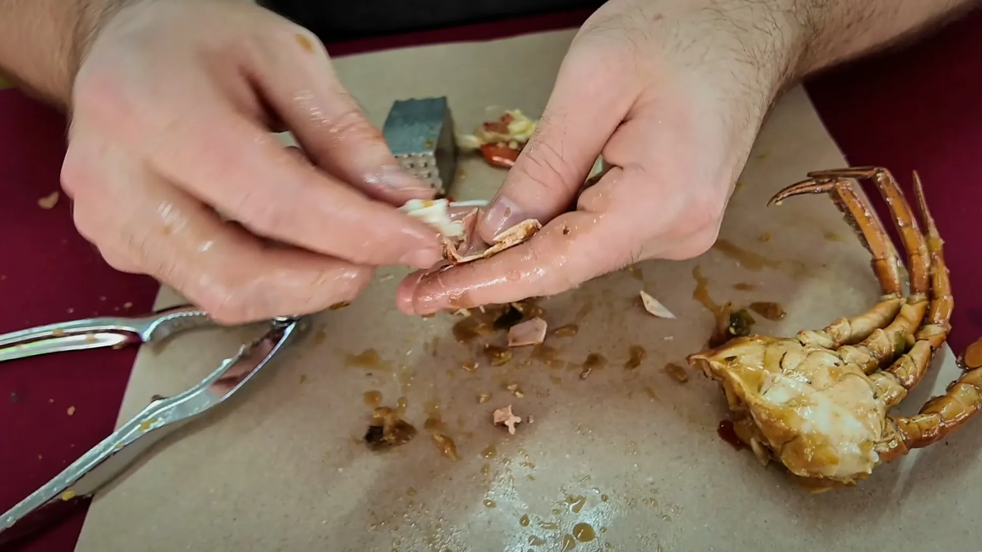 Hands picking crab meat out of a cracked shell over a sheet of paper at Fatty Crab, Petaling Jaya.