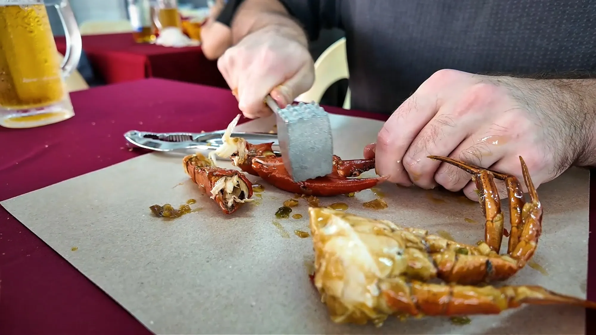 Cracking a crab leg with a small metal mallet on a sheet of paper at Fatty Crab, with a glass of beer behind.