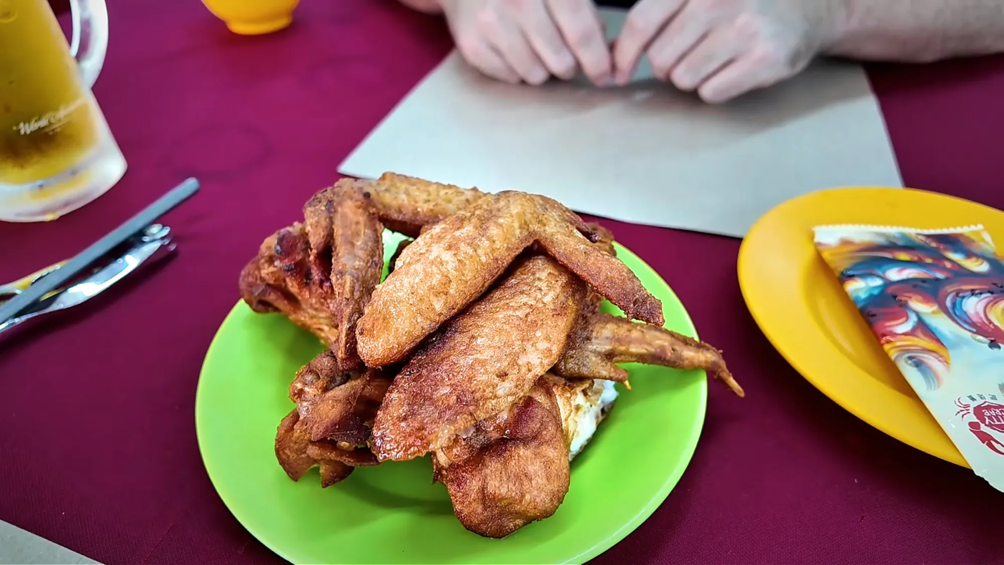 A green plate of crispy fried chicken wings on a red tablecloth at Restoran Fatty Crab, Petaling Jaya.