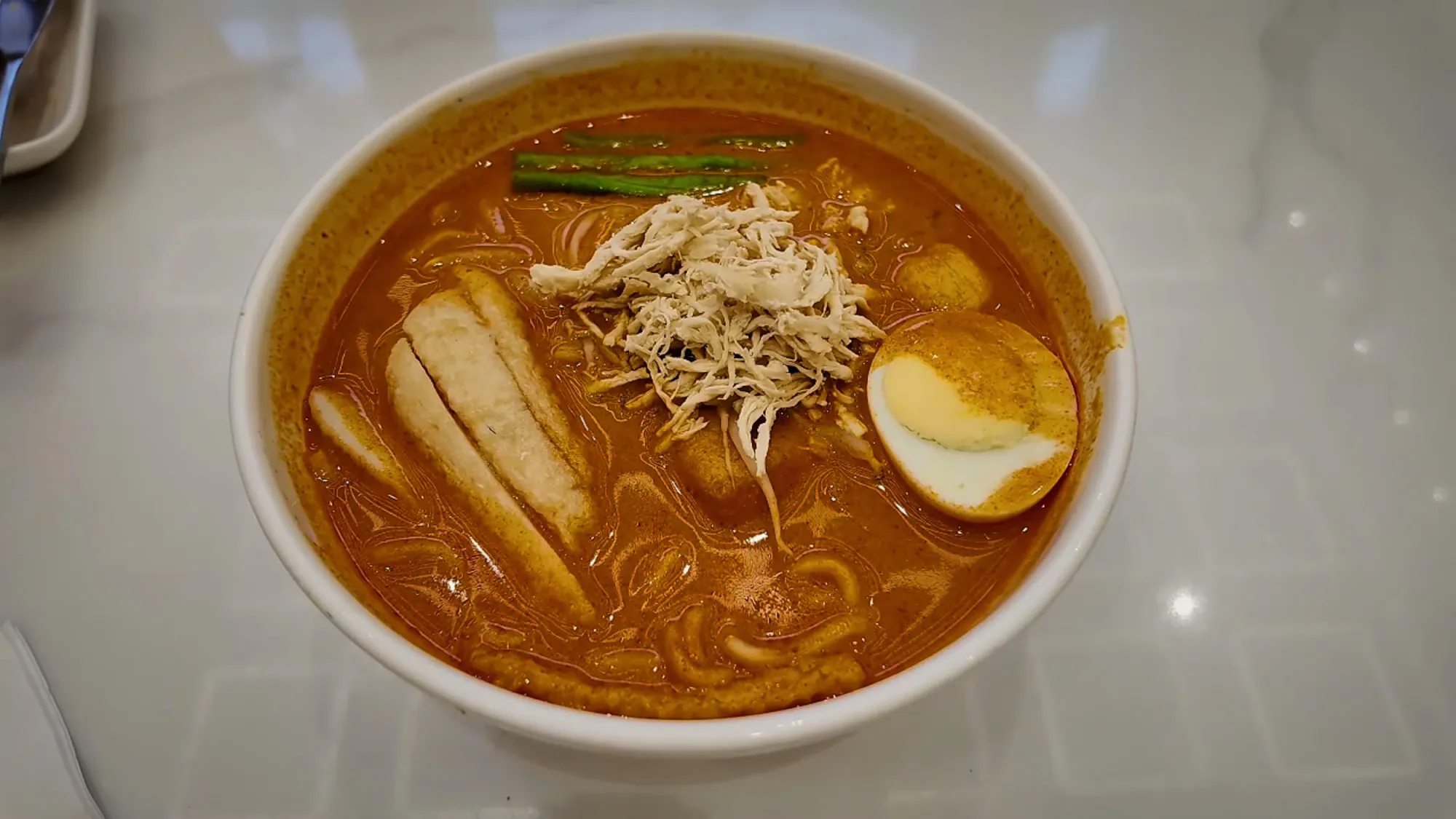 A bowl of curry laksa with chicken, fish cake, and a boiled egg at Oriental Kopi.
