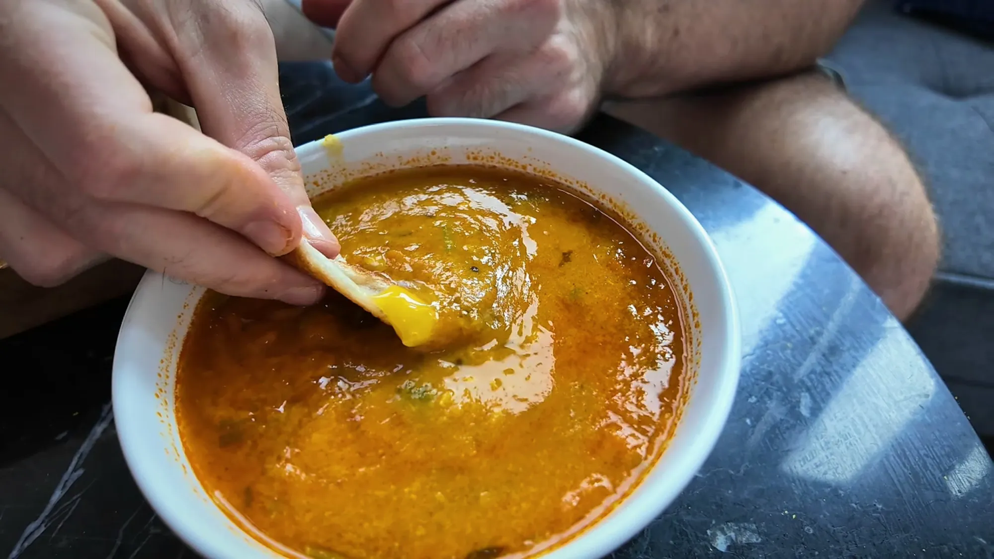 A piece of bird's nest roti with egg yolk on it being dipped into a bowl of dhal