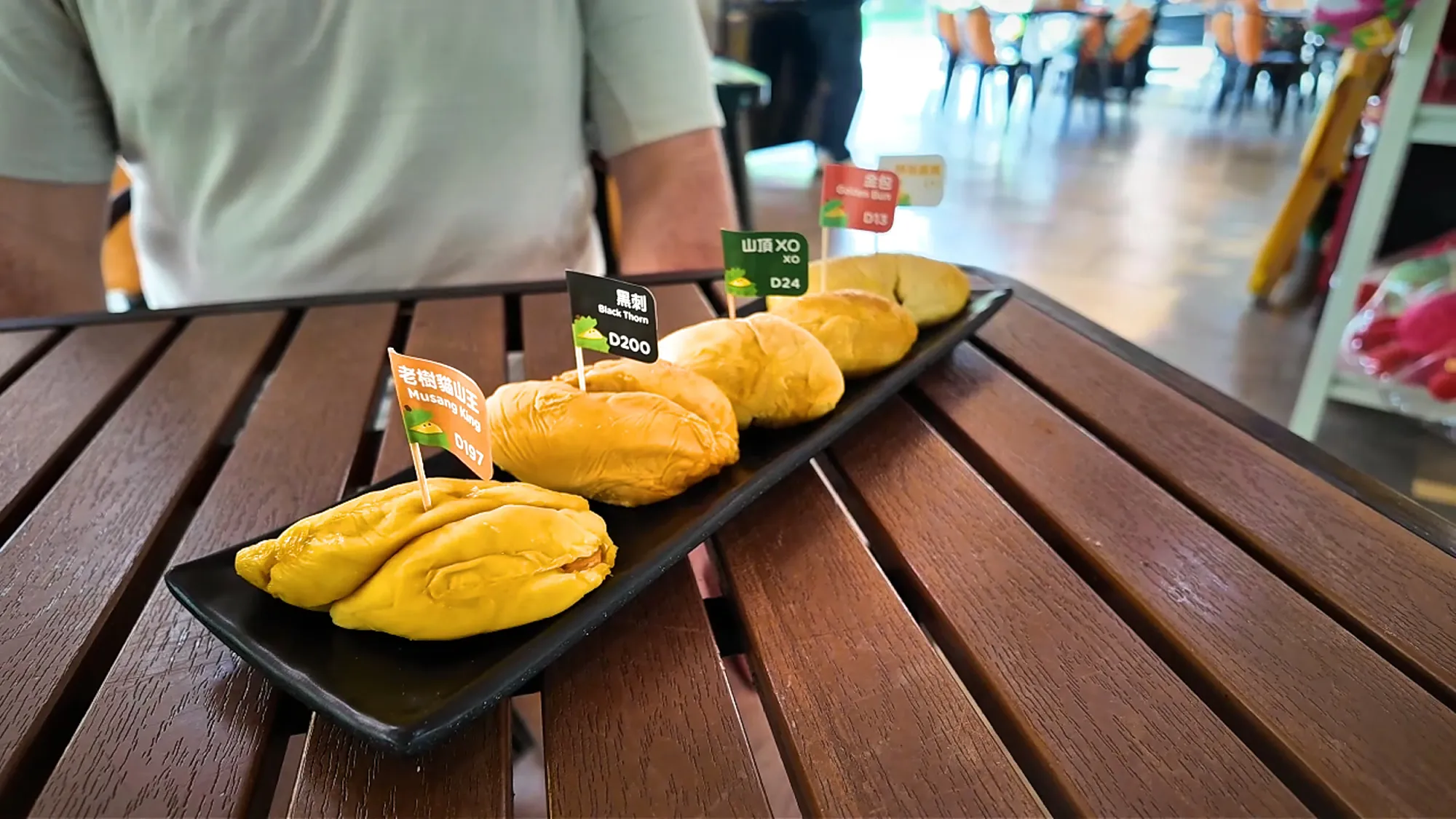 Five flagged durian pieces lined up on a long black platter at DurianBB Park, Kuala Lumpur."