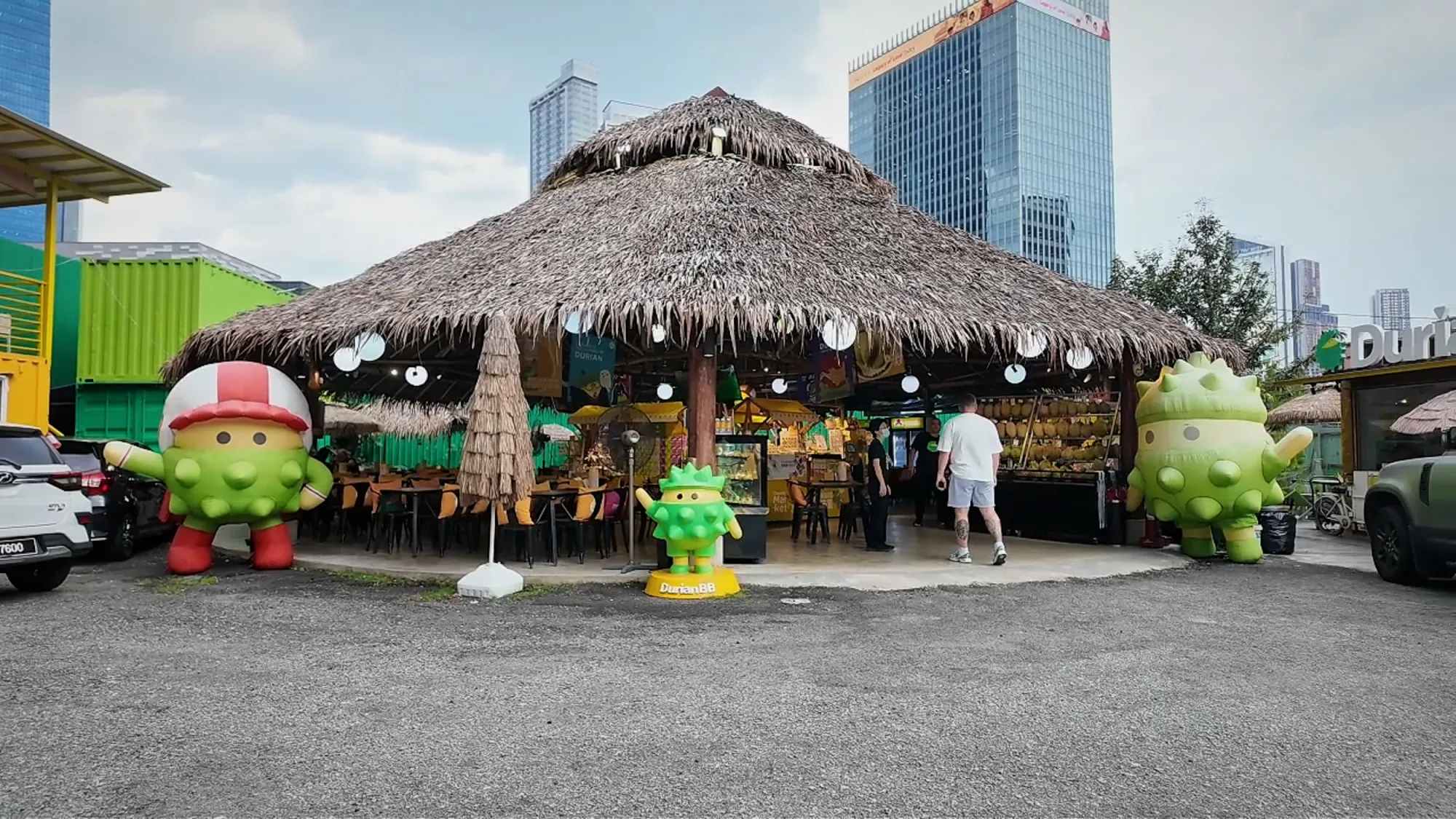 The outside of DurianBB Park in Kuala Lumpur, with a thatched pavilion and giant inflatable durian mascots.