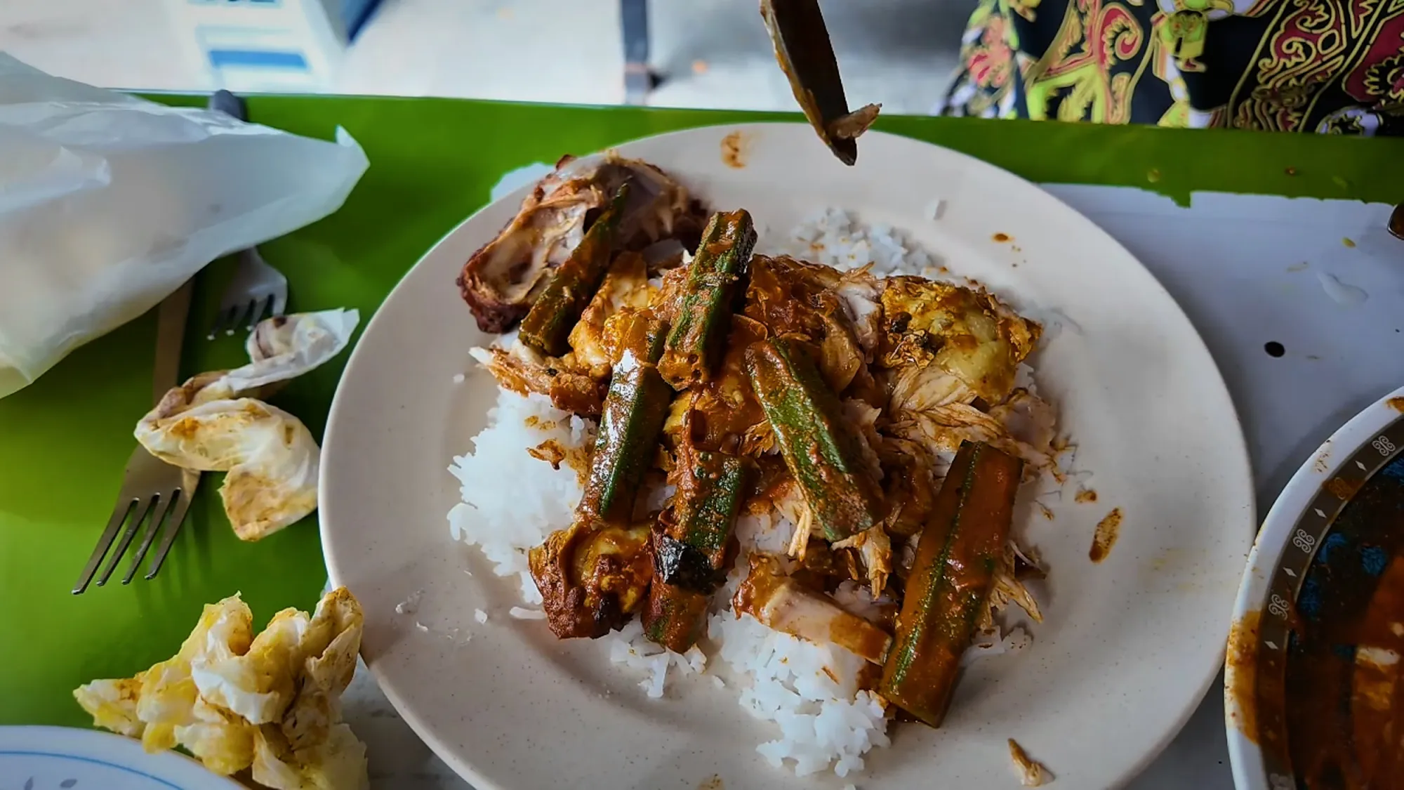 Pieces of fish and okra in curry spooned over white rice on a plate at Anuar Curry Fish Head in Kuala Lumpur.