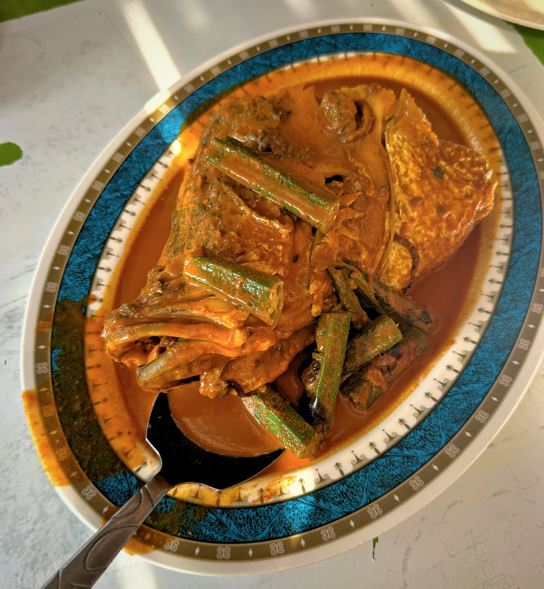A large fish head curry smothered in rich spiced gravy with okra served on a decorative oval platter in Brickfields, Kuala Lumpur.
