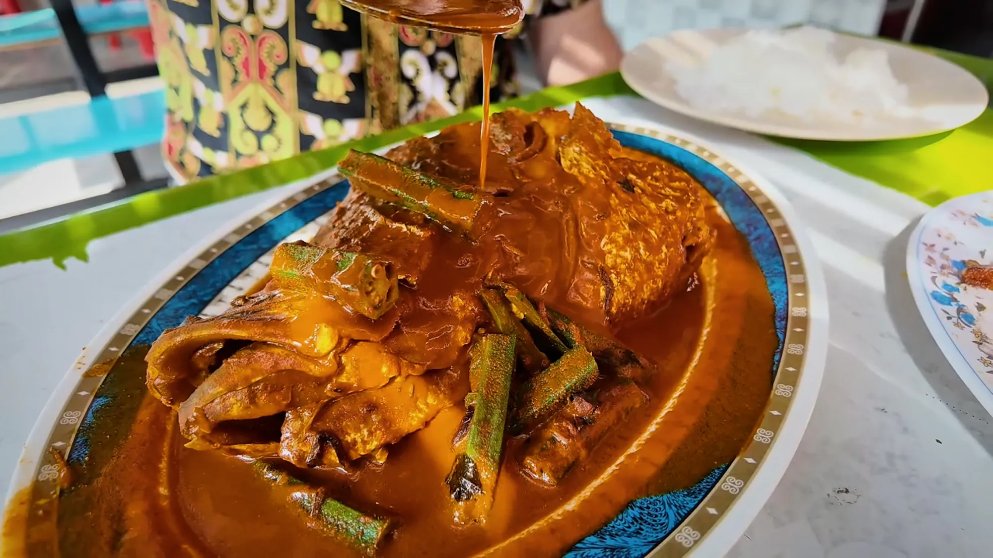 A whole fish head in red curry with okra on a blue-and-gold rimmed platter at Anuar Curry Fish Head in Bangsar, Kuala Lumpur.
