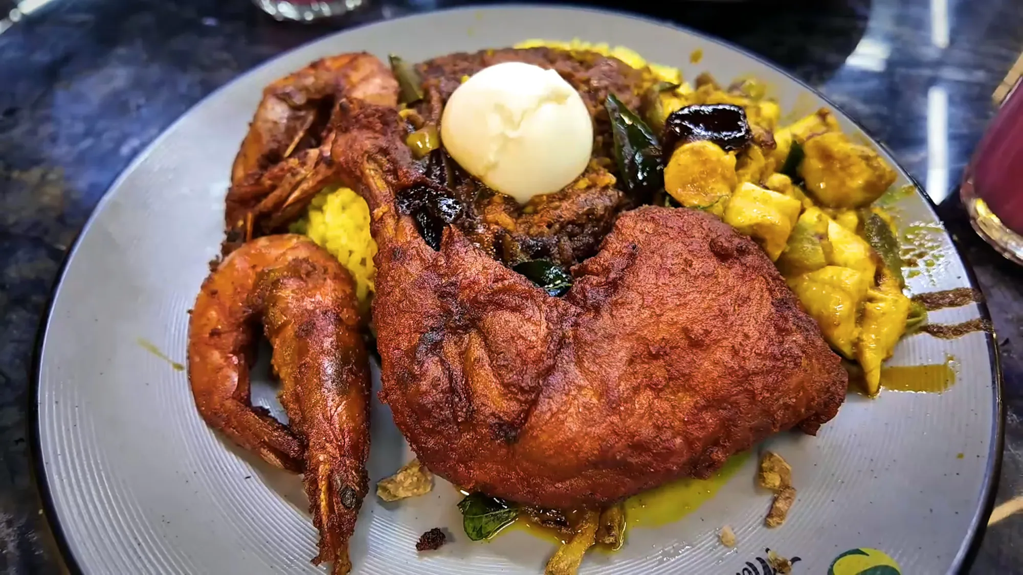 A close-up of nasi kandar at Saddam Nasi Kandar in Kuala Lumpur: a whole fried chicken leg, tiger prawns, a boiled egg, and curry over yellow rice.