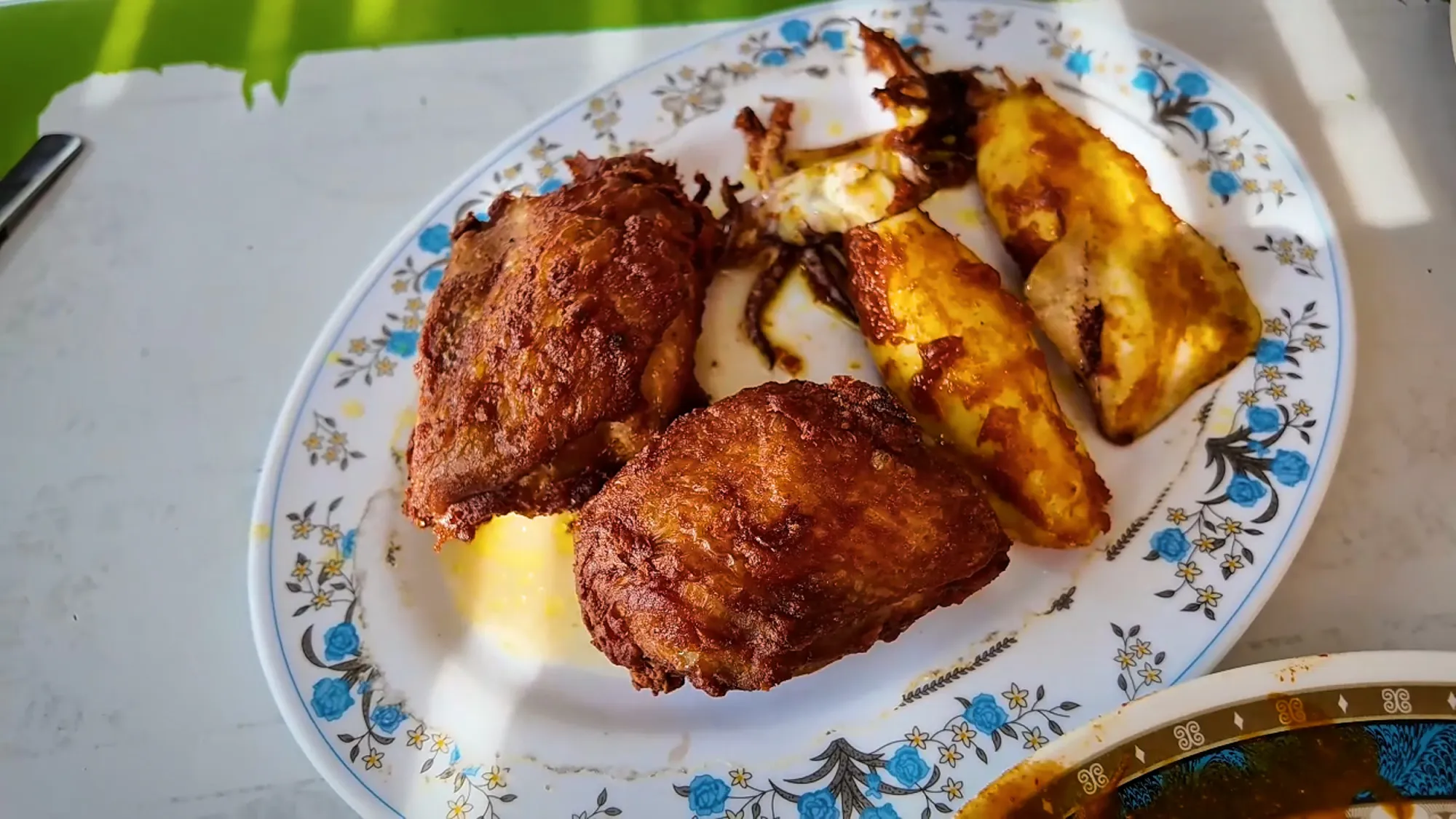 Two pieces of crispy fried chicken and pieces of fried squid on a blue floral plate at Anuar Curry Fish Head in Bangsar, Kuala Lumpur.