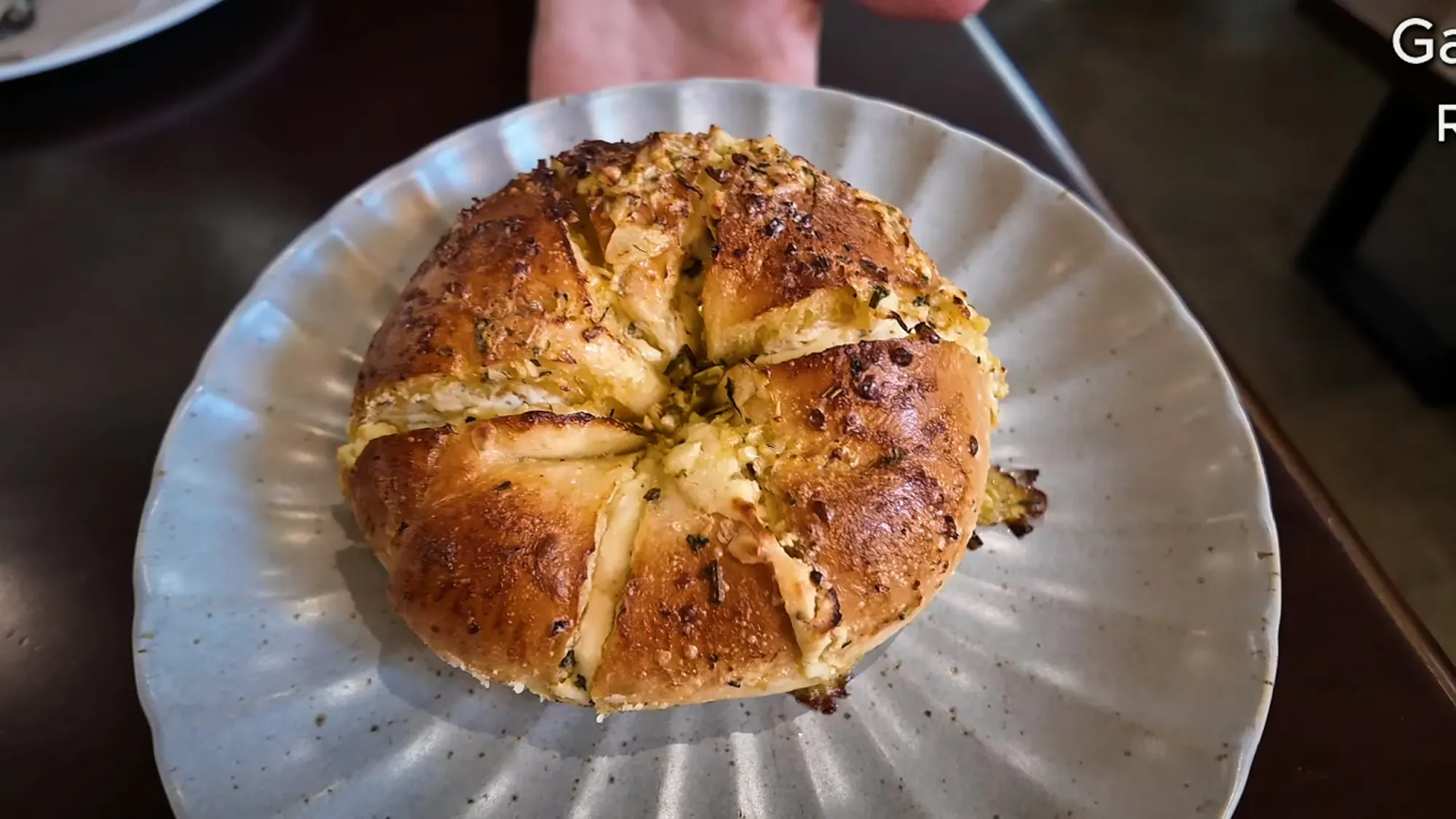 Round garlic bagel with a golden roasted garlic topping scored into wedges, on a white scalloped plate.